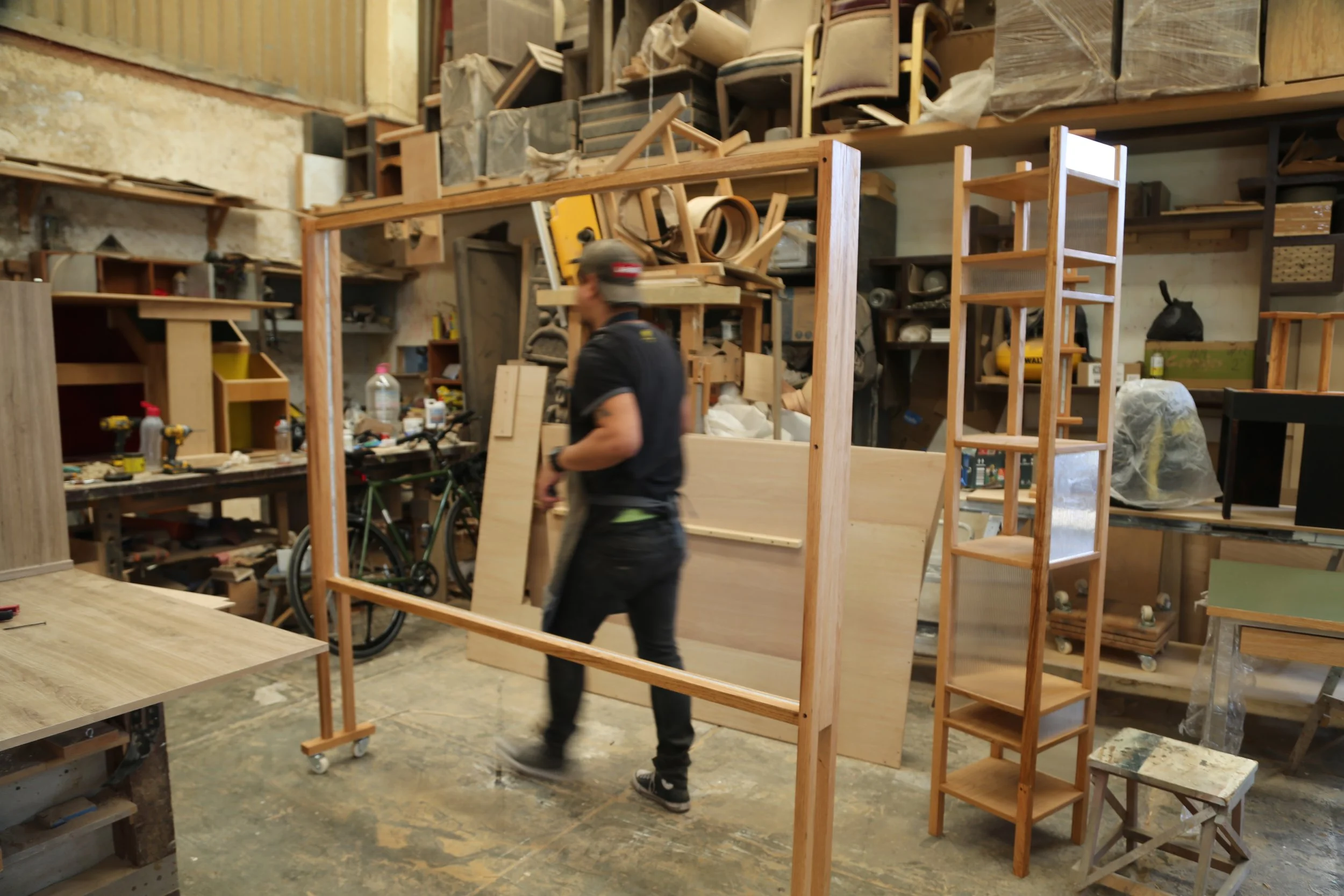 A member of our team walking past wooden furniture and shelving inside a woodworking shop