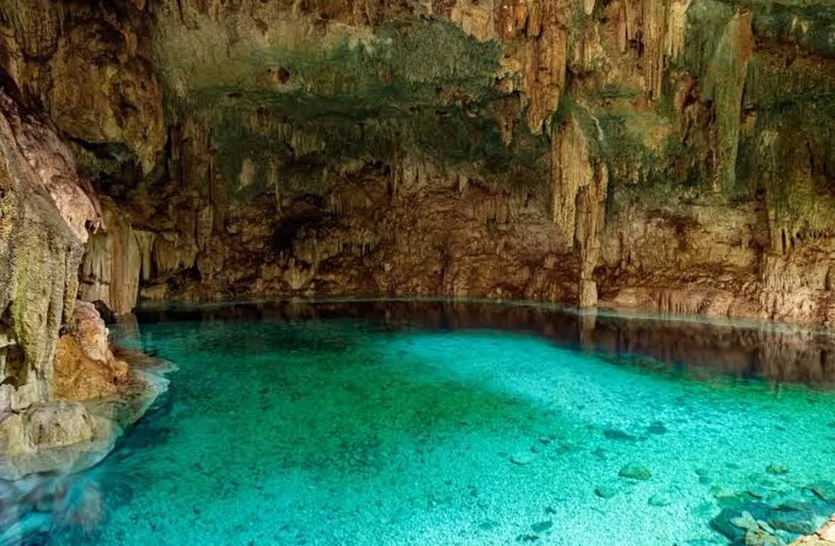 Inside a cave with turquoise water and rocky walls with stalactites and stalagmites.
