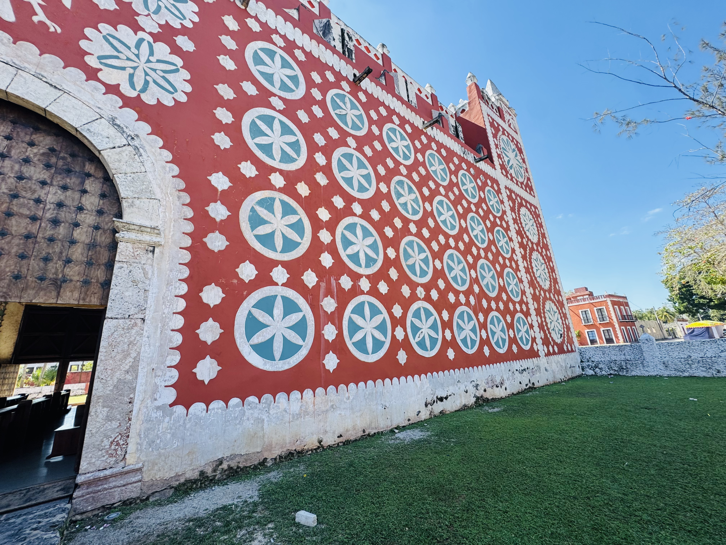 A colorful building with a red wall decorated with white and blue geometric patterns and circles, featuring arched openings with stone accents, under a clear blue sky.