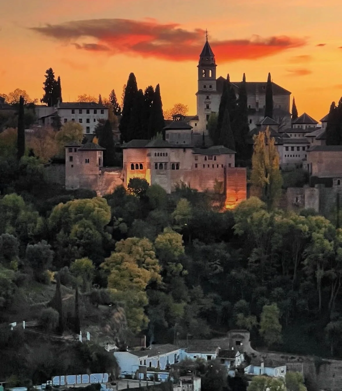 Sunset over a historic hilltop village with a castle, church, and lush trees.
