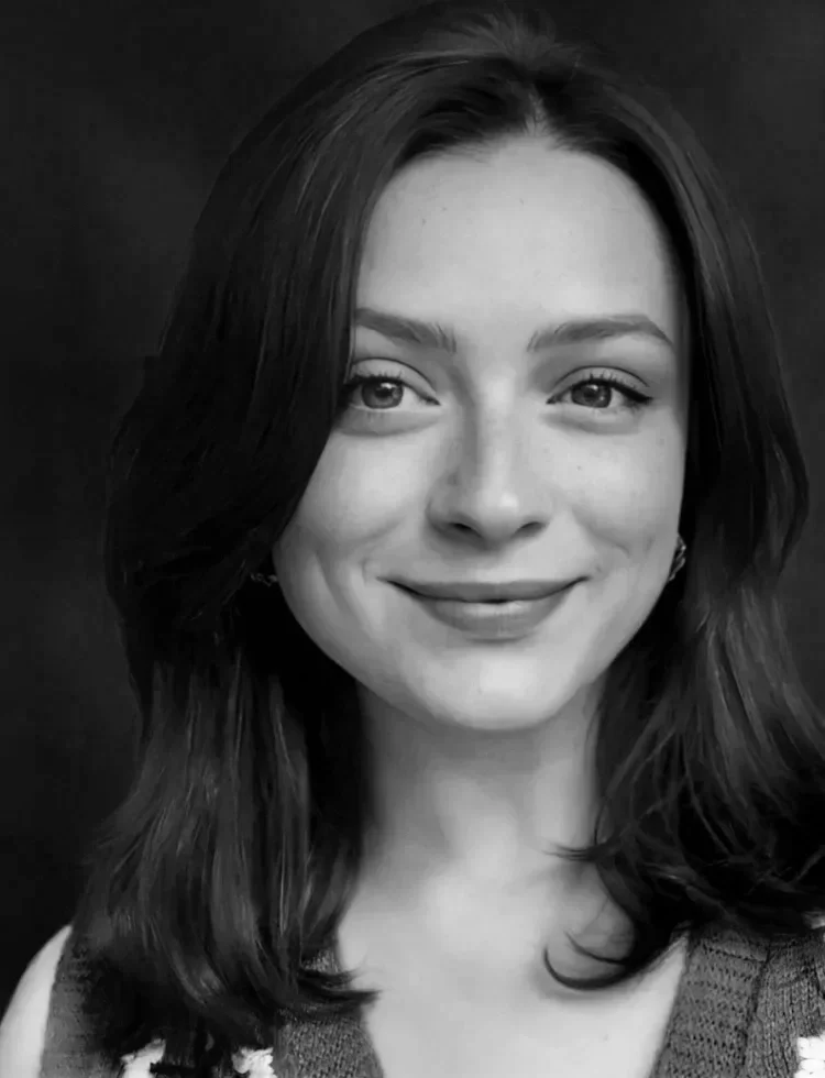 Close-up black-and-white portrait of a smiling woman with shoulder-length dark hair, wearing a sleeveless top, against a dark background.