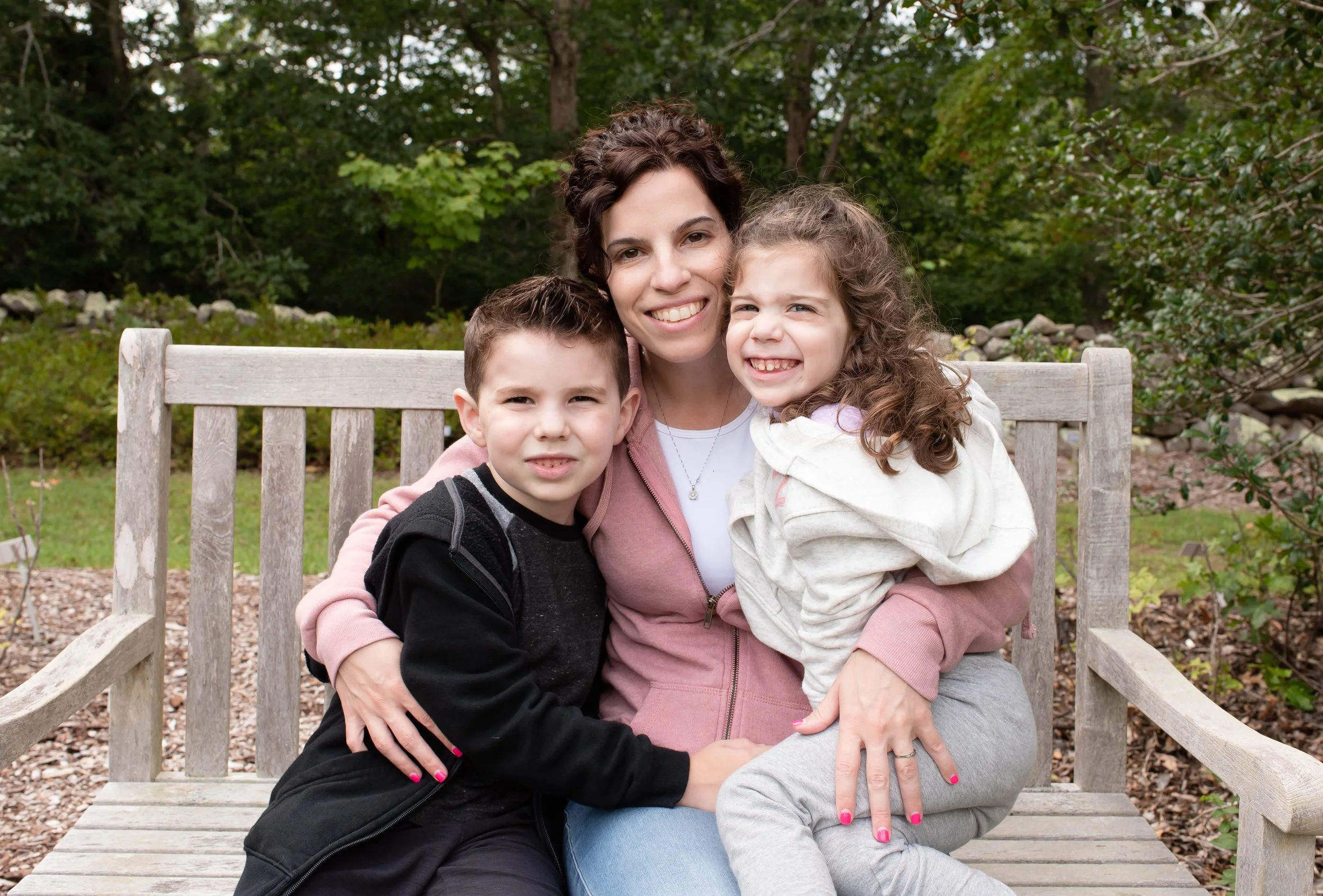 Mother sitting on a park bench with her two children during a natural light family photography session in New Jersey