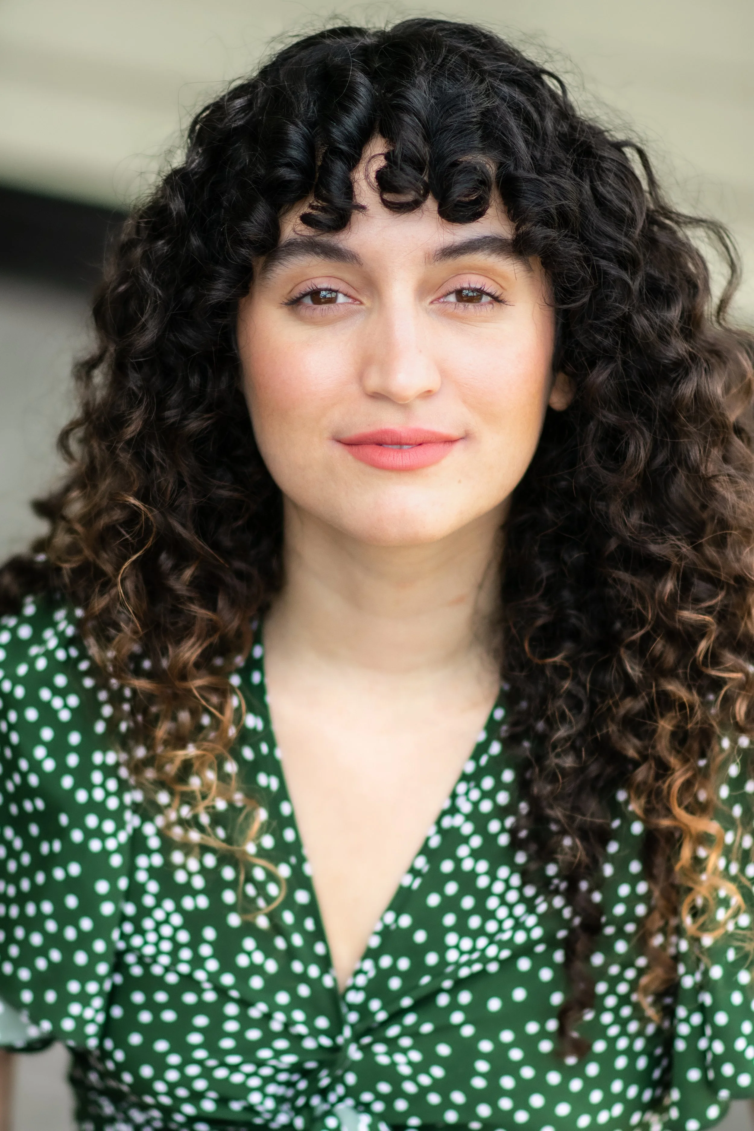 Close-up portrait of a woman with curly dark hair wearing a green dress with white polka dots.