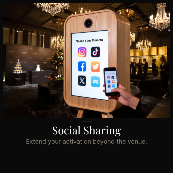 A digital screen on a wooden stand showing social media icons for Instagram, TikTok, Facebook, Twitter, and others, with a person holding a smartphone in front of it. The background appears to be an elegant event venue with chandeliers and people socializing.