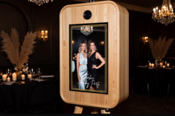 A photo booth with a wooden frame displaying two women dressed up for a party, in a venue decorated with candles and chandeliers.