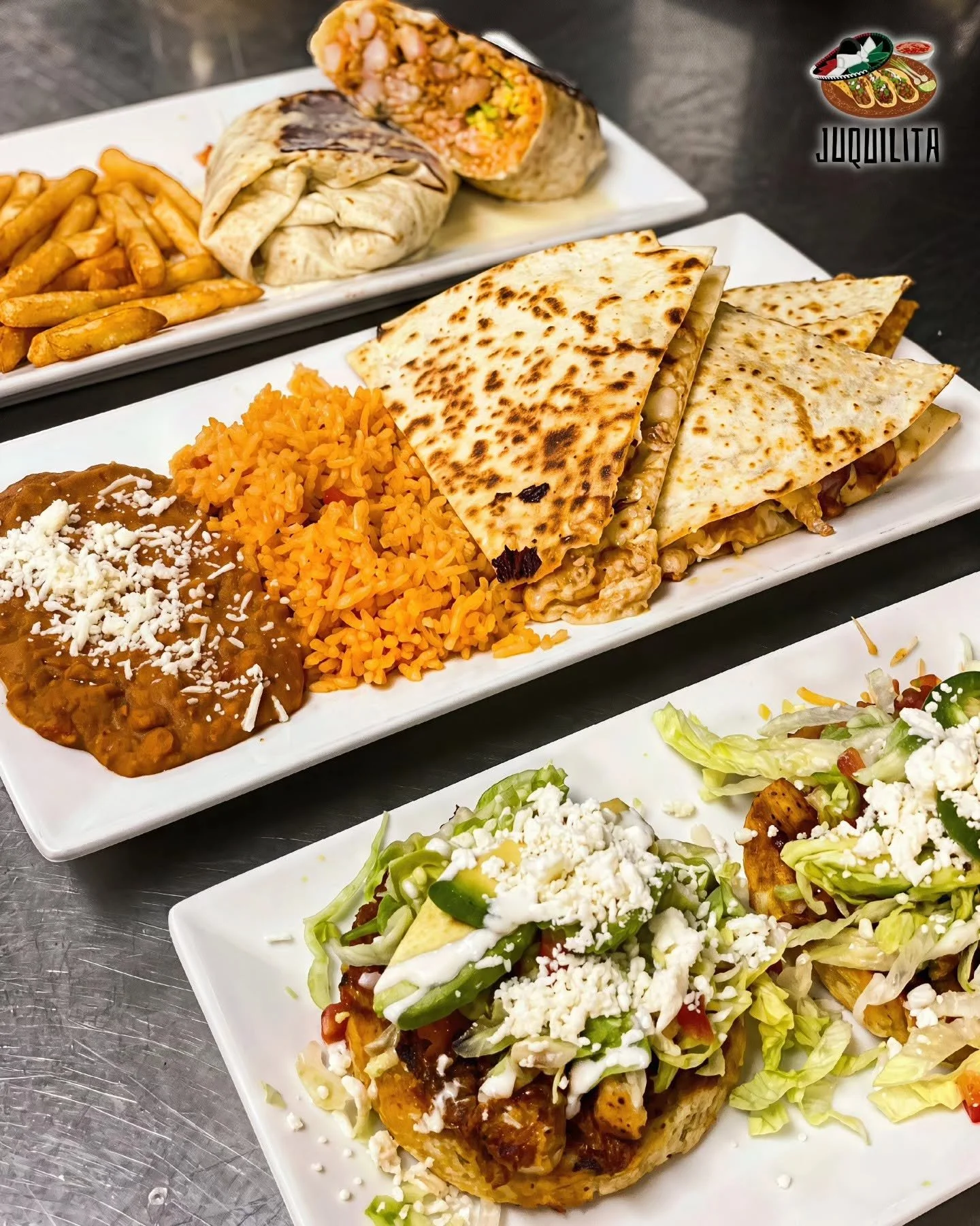 Close-up of three plates of Mexican food on a metallic surface. The front plate features a burrito cut in half with rice, beans, and shredded cheese on the side. The middle plate has quesadillas cut into triangles. The background plate contains Frenc
