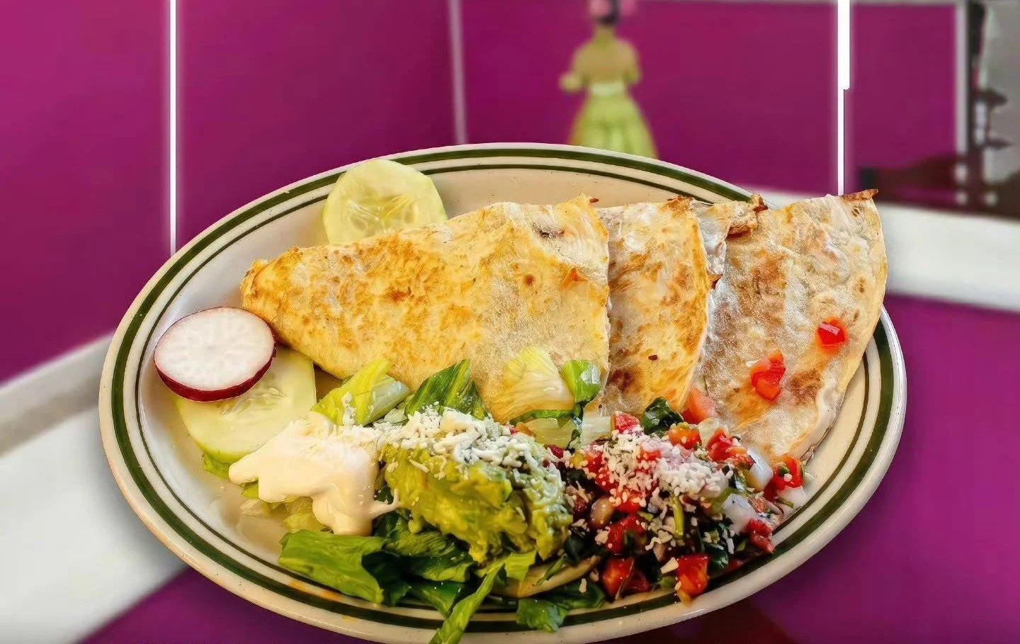 A plate of Mexican food with two quesadillas, a side salad, sliced radish, cucumber, and lemon in the background, set against a purple background.