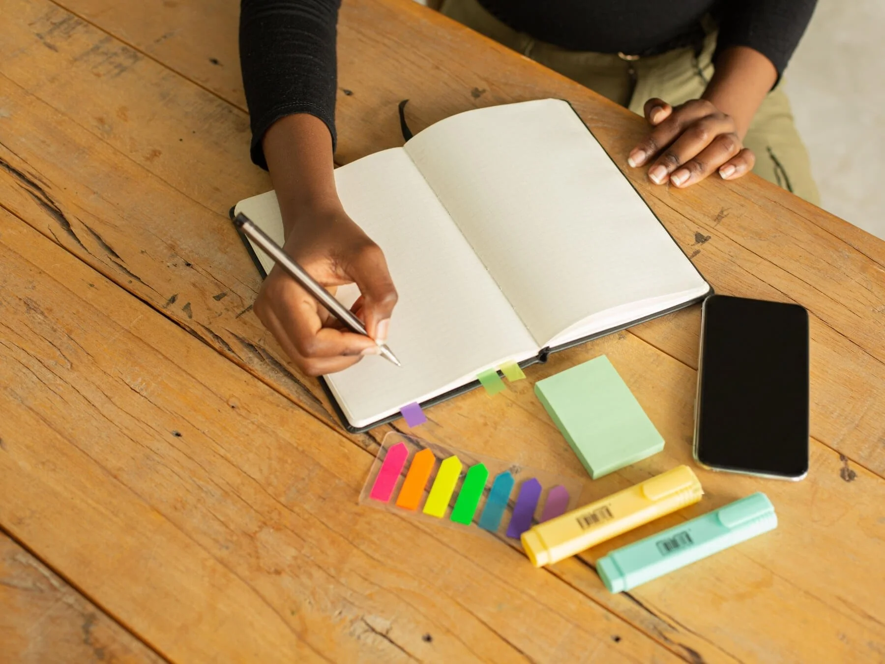 Hand writing in a notebook surrounded by highlighters and organizing tools, reflecting the pull to keep everything straight.