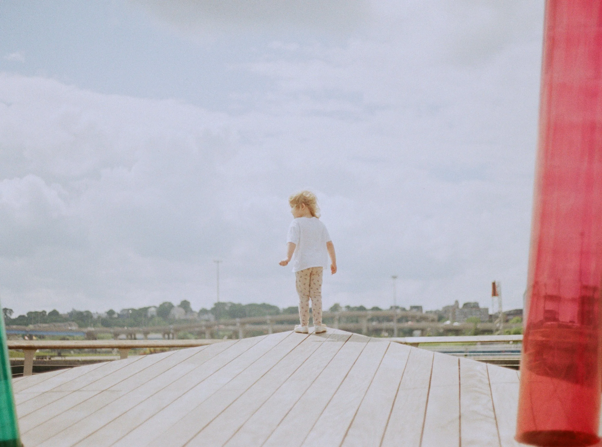 A young girl with blonde hair, wearing a white shirt and patterned pants, standing on a curved rooftop.