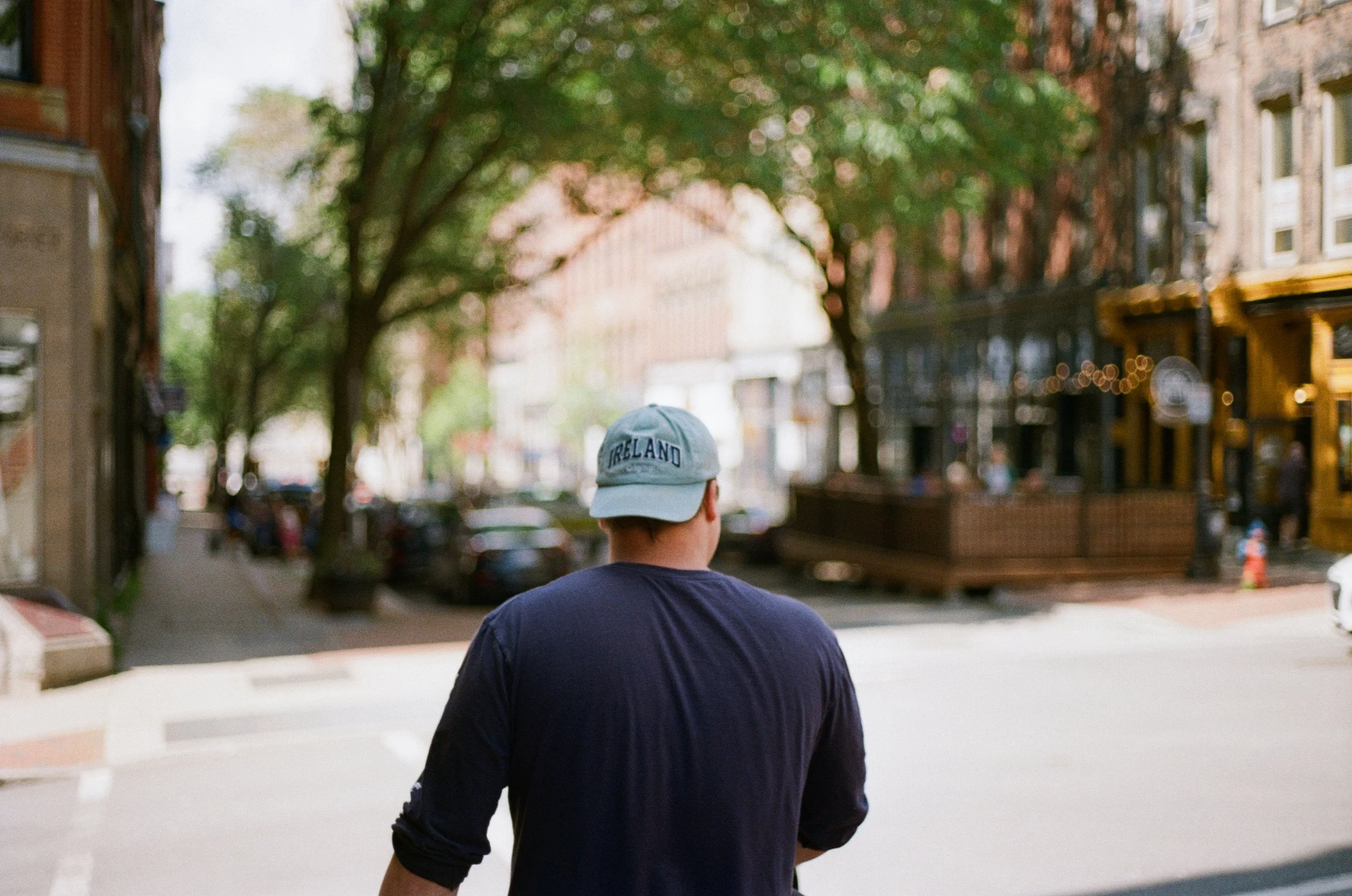 A person wearing a gray cap with a navy shirt walking down a city street.