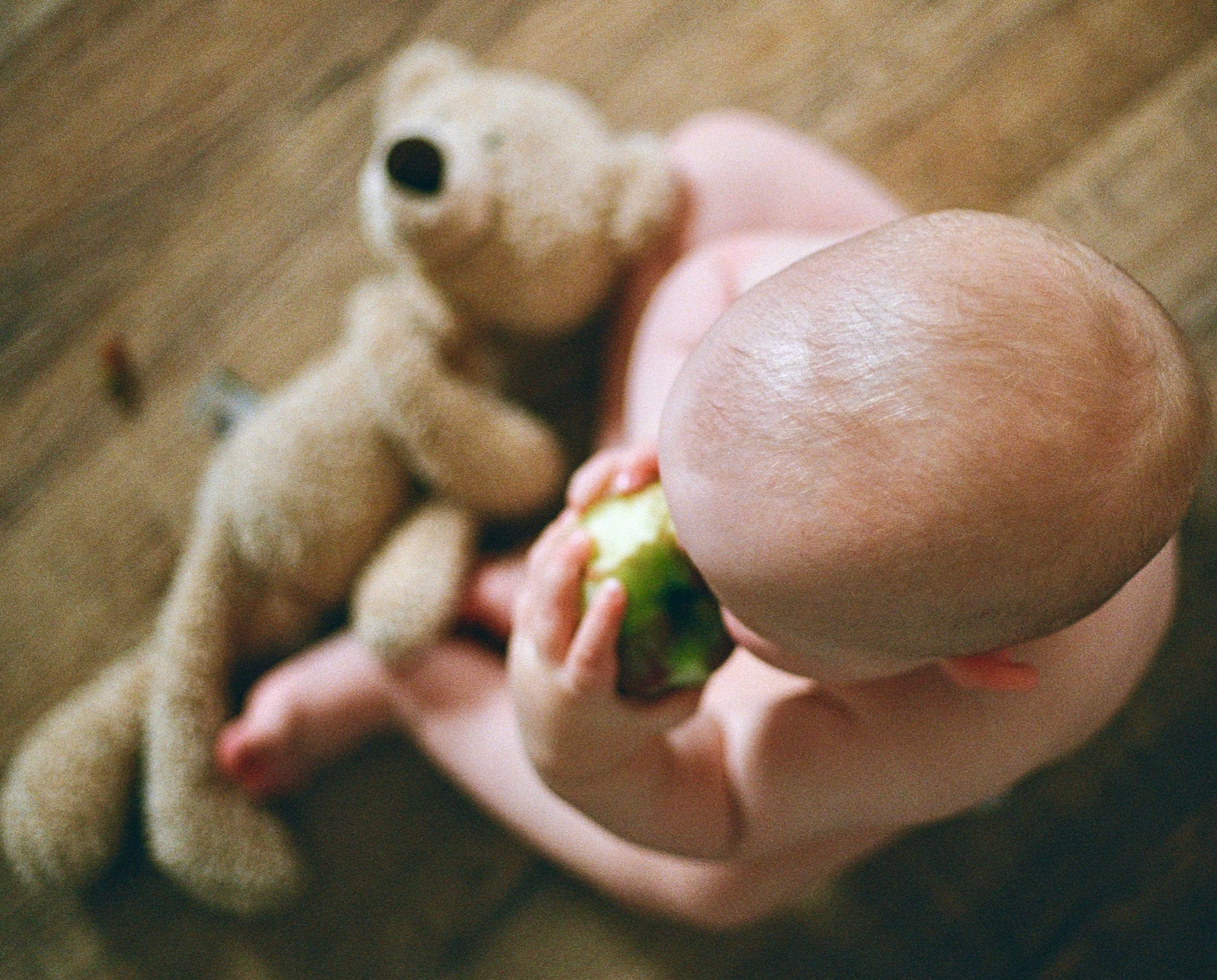 Close-up of a child's hand holding an apple and a blurred teddy bear in the background.