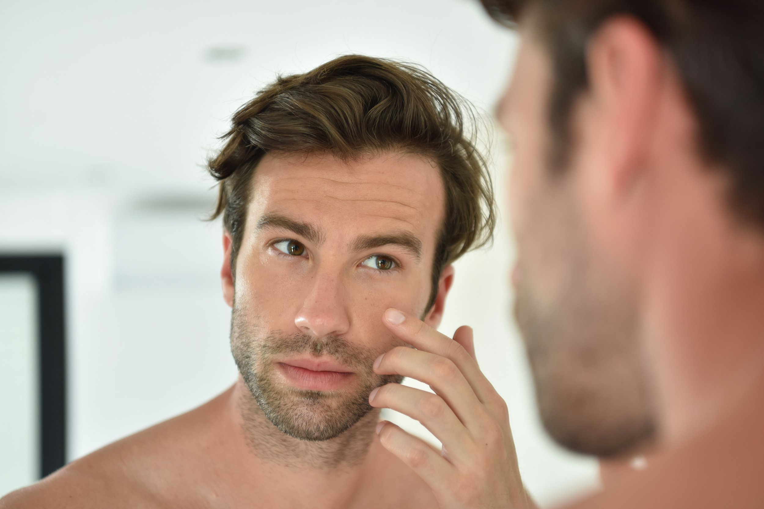 A shirtless man with brown hair and a beard looks at a person who is out of focus in the foreground.