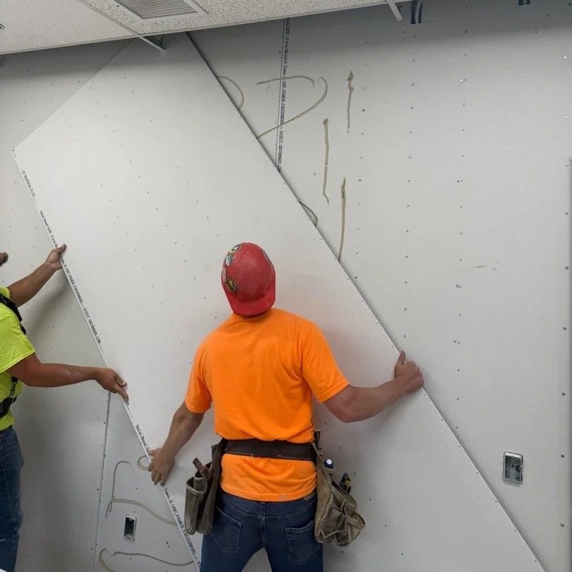 Construction workers installing drywall on a ceiling wall.