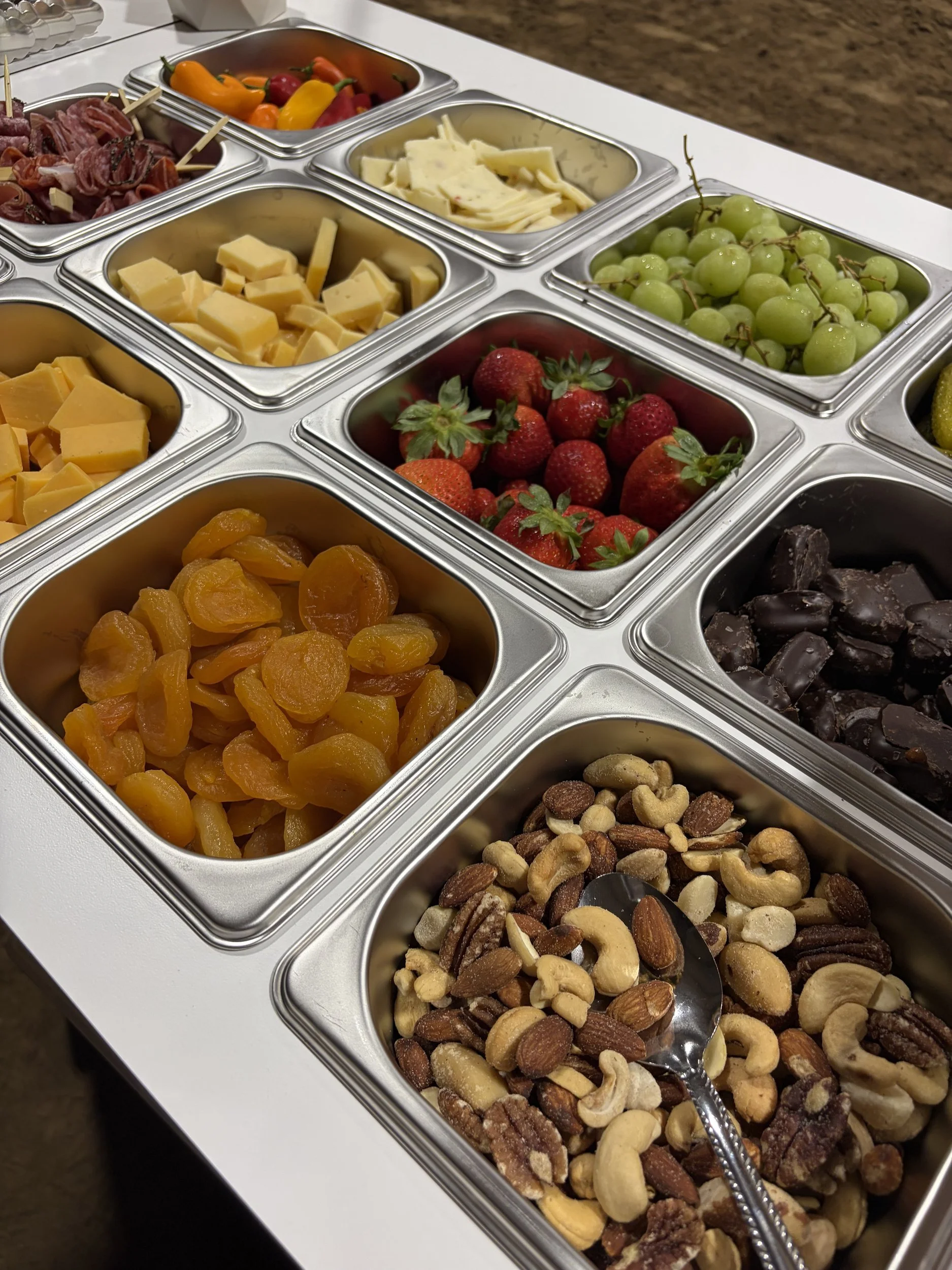 Charcuterie cart wells filled with mixed nuts, dried apricots, strawberries, green grapes, chocolate pieces, sliced cheeses and cured meats