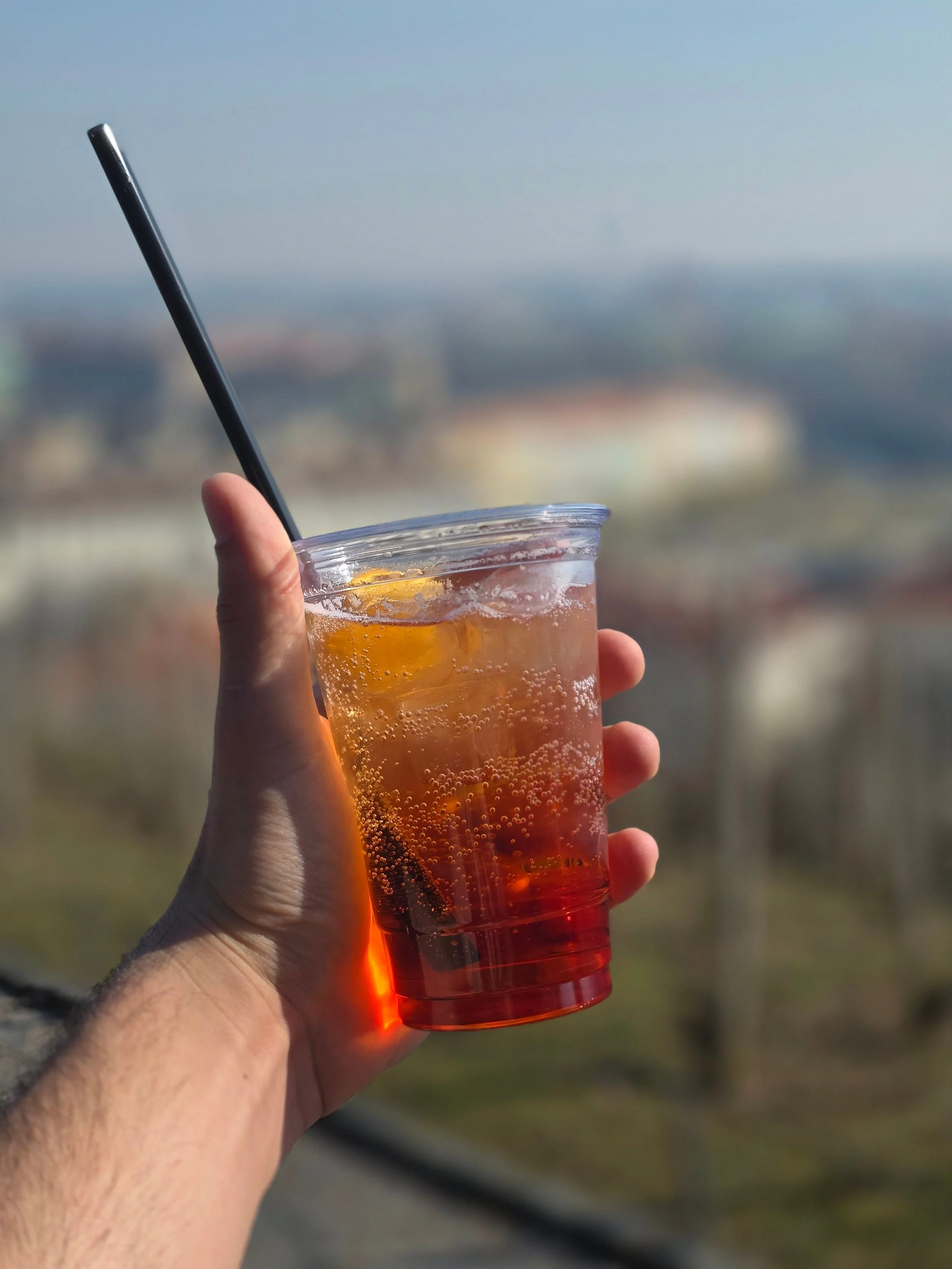 Hand holding an iced Aperol spritz cocktail with a city skyline in the background