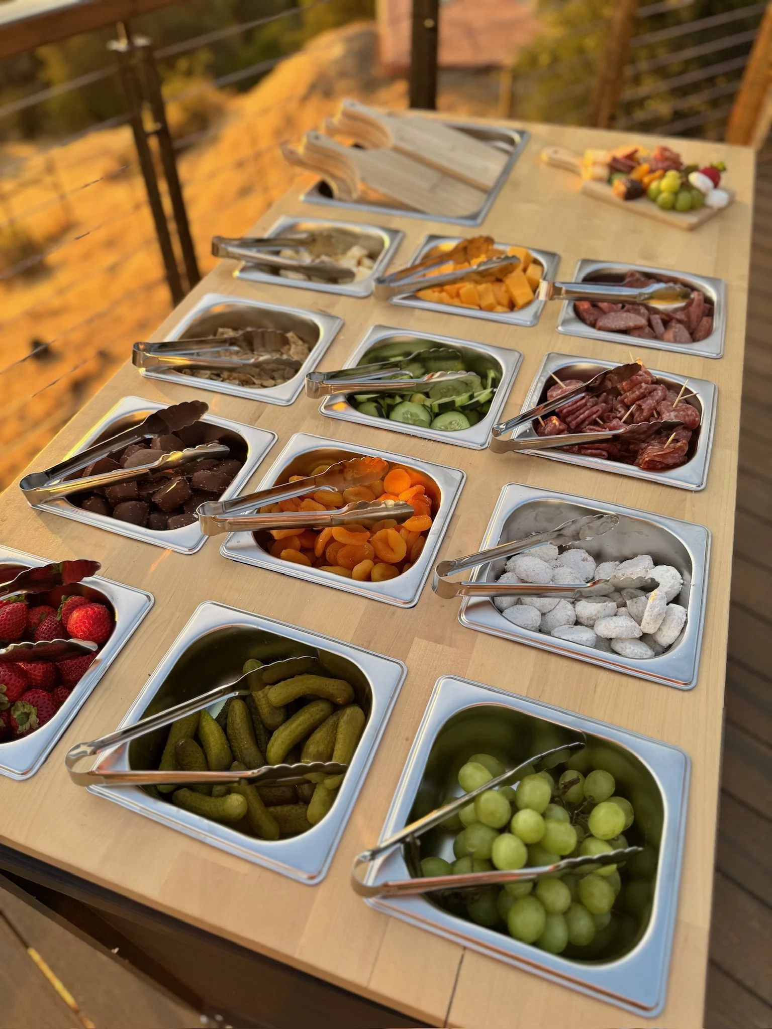 Charcuterie cart with metal trays of assorted meats, cheeses, and vegetables set up outdoors at dusk