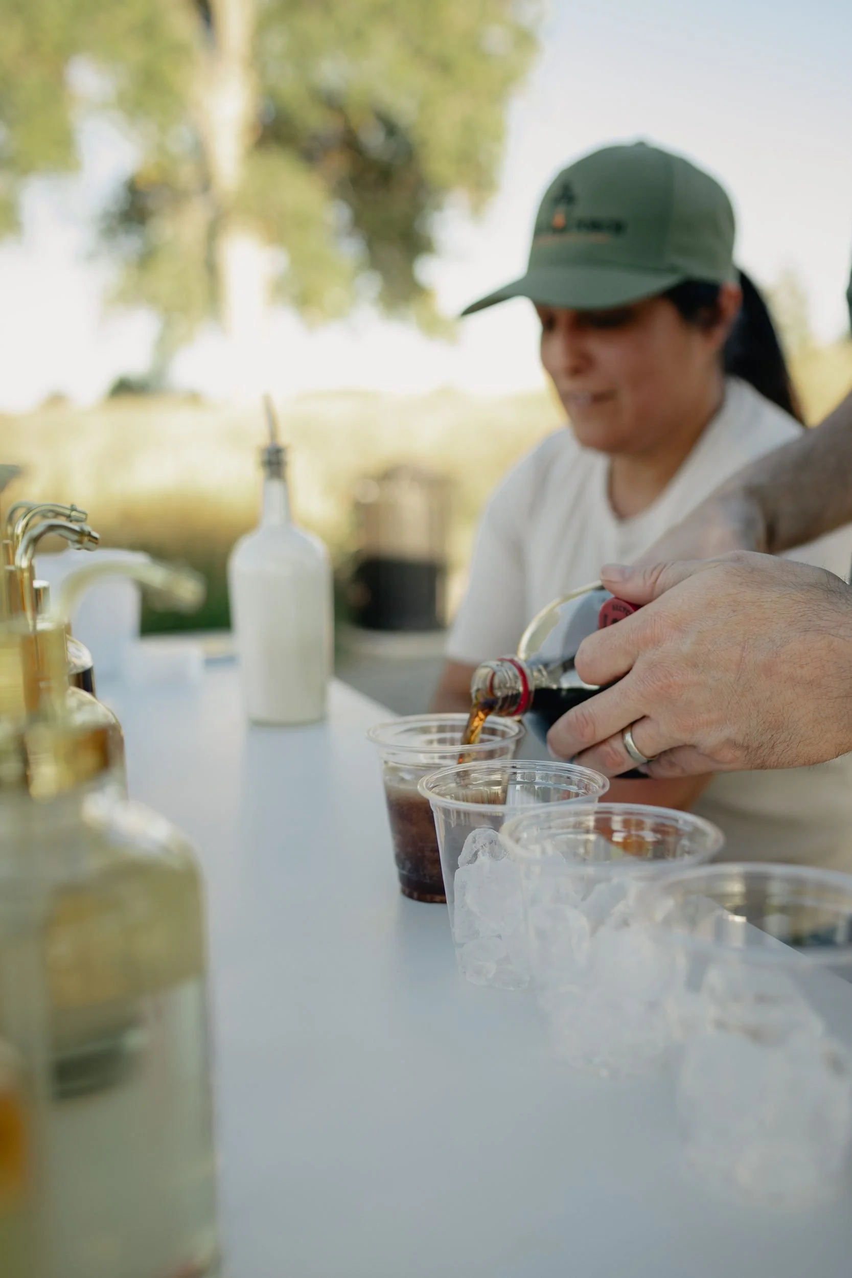 Soda being poured into a row of iced cups at the Front Porch Social Dirty Soda Bar, with a server in a green cap in the background