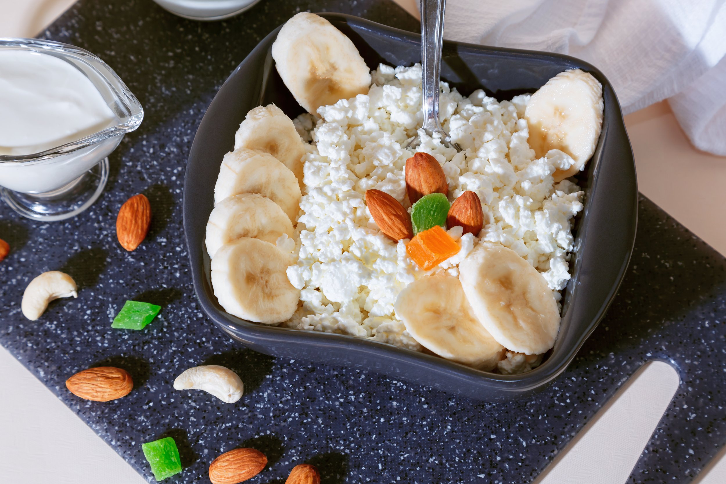 Cottage cheese in a bowl with a spoon, garnished with bananas, nuts, and candied fruits, part of Front Porch Social's Protein Power Bar catering service in Northern Colorado