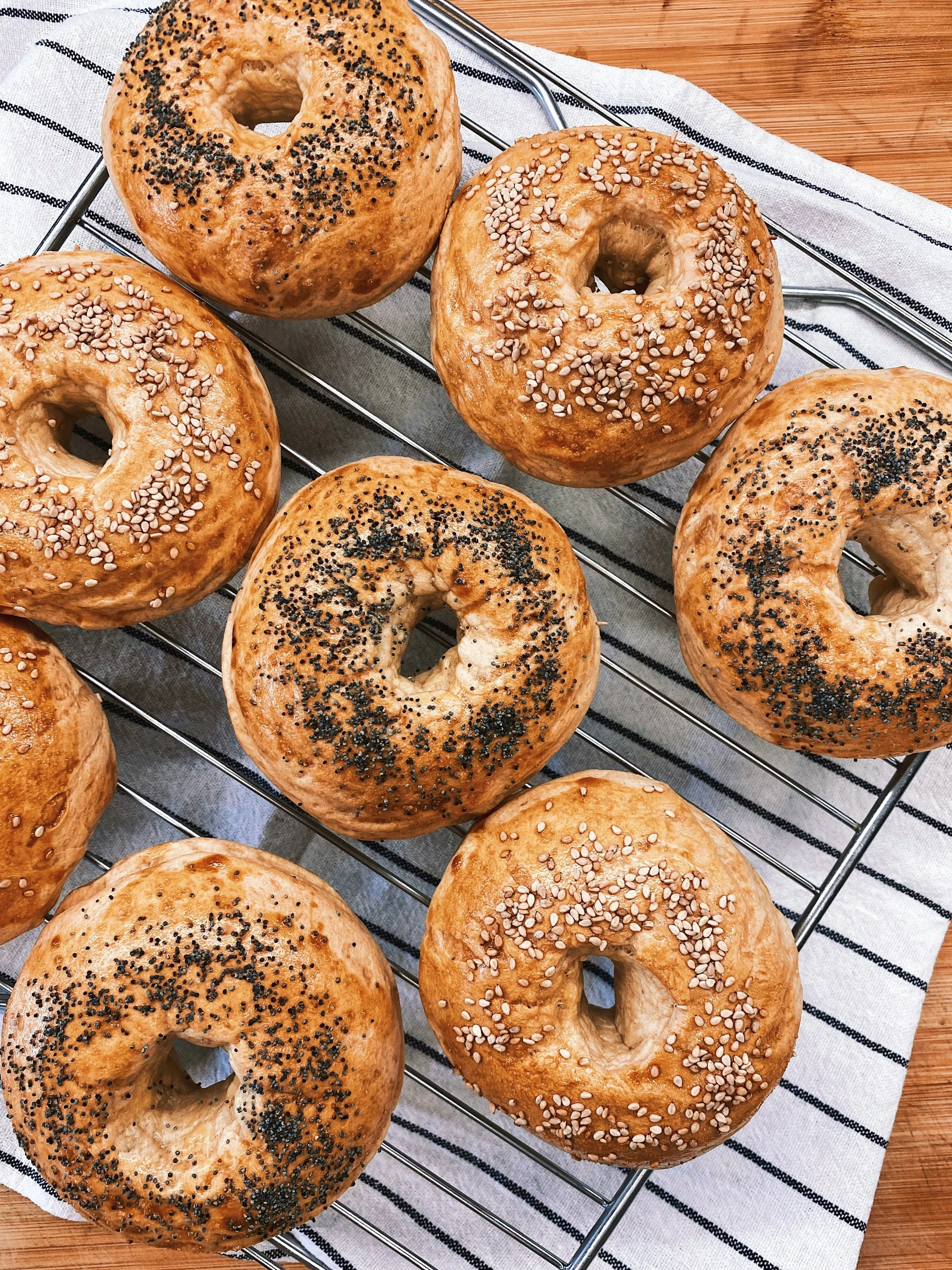 Assorted bagels topped with sesame and poppy seeds cooling on a wire rack