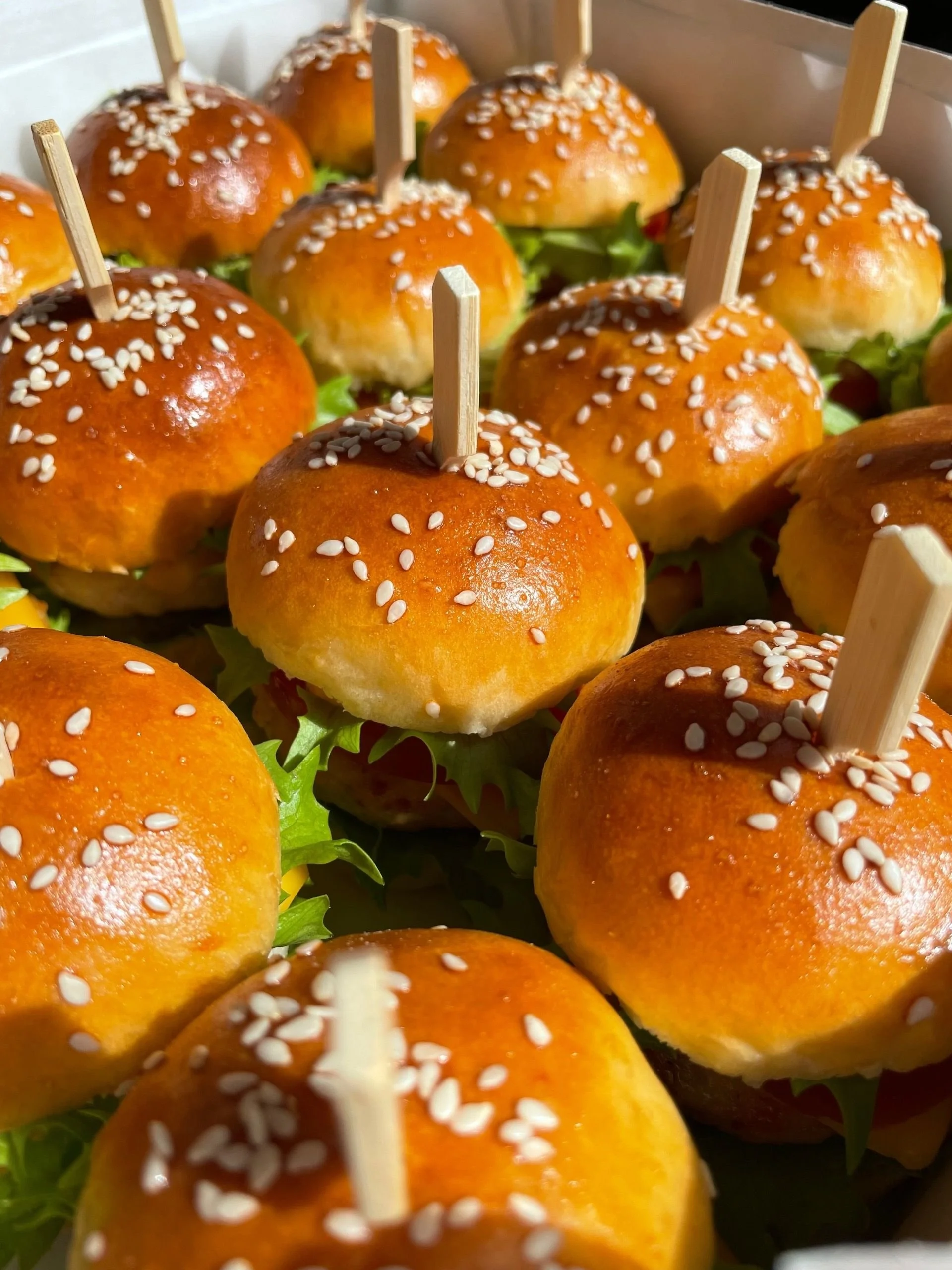 Golden brown sourdough slider buns with sesame seeds skewered on picks