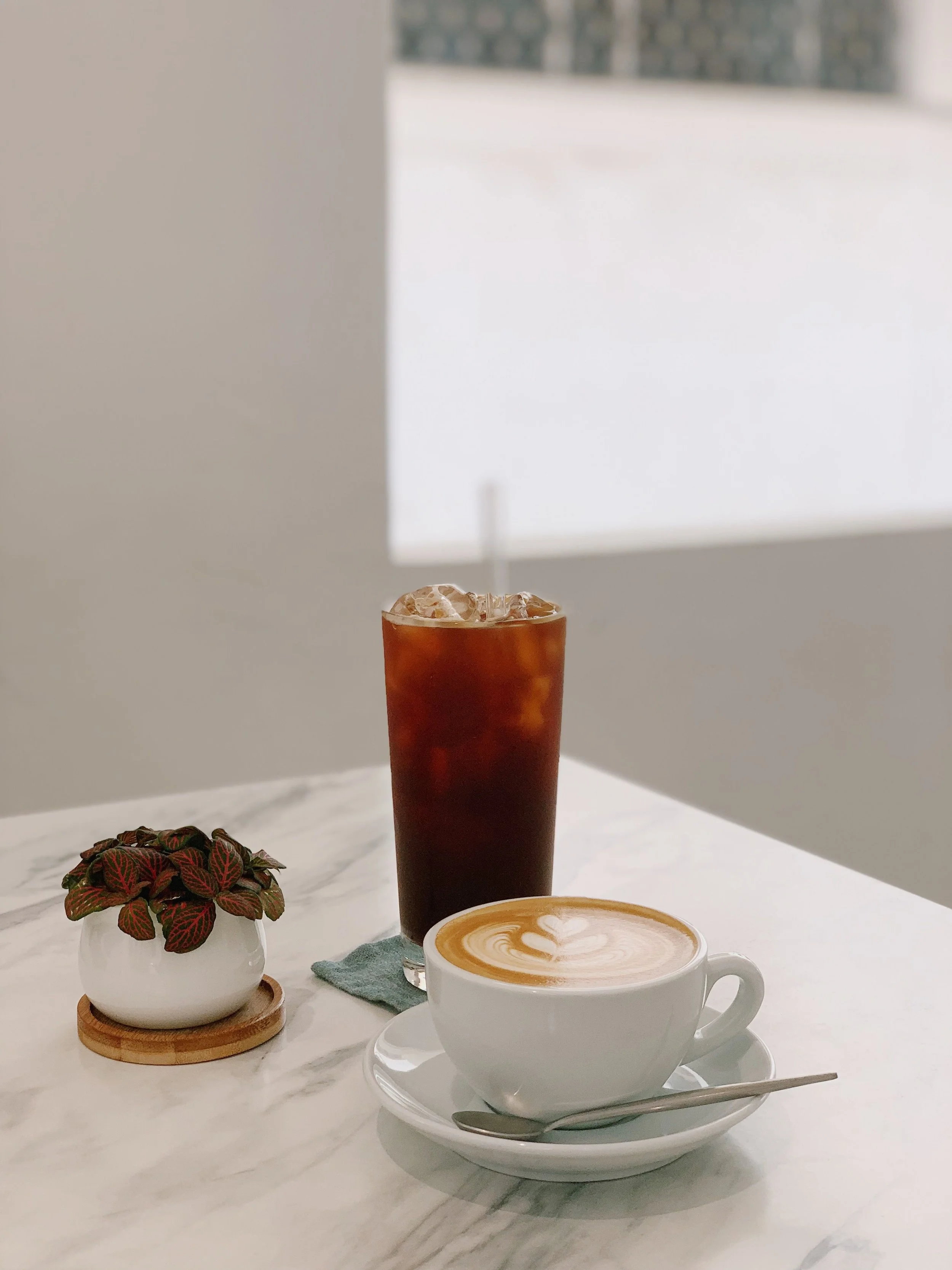 Iced coffee and latte with heart-shaped foam art on a marble table, part of Front Porch Social's mobile Coffee & Tea Cart catering service in Northern Colorado