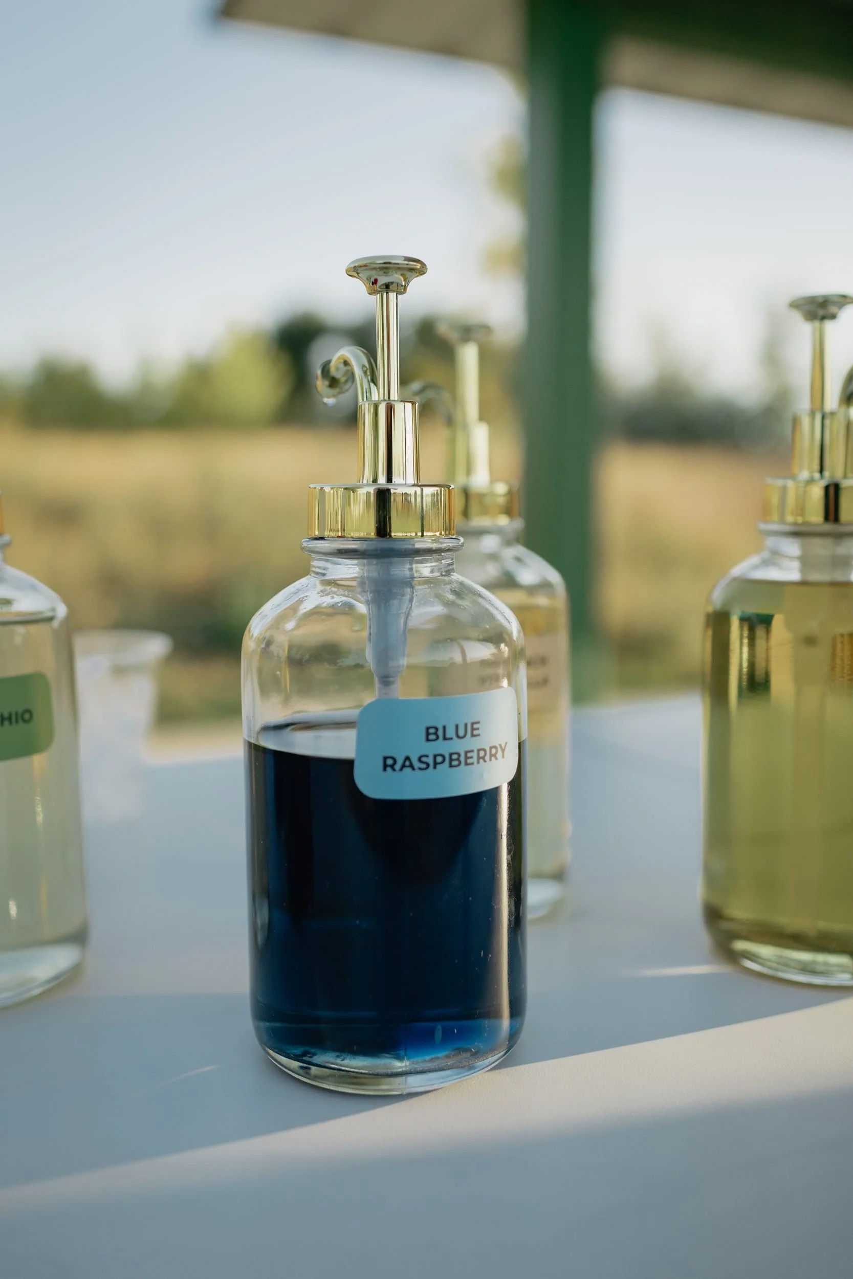 Blue raspberry syrup bottle with a gold pump on the Front Porch Social Dirty Soda Bar