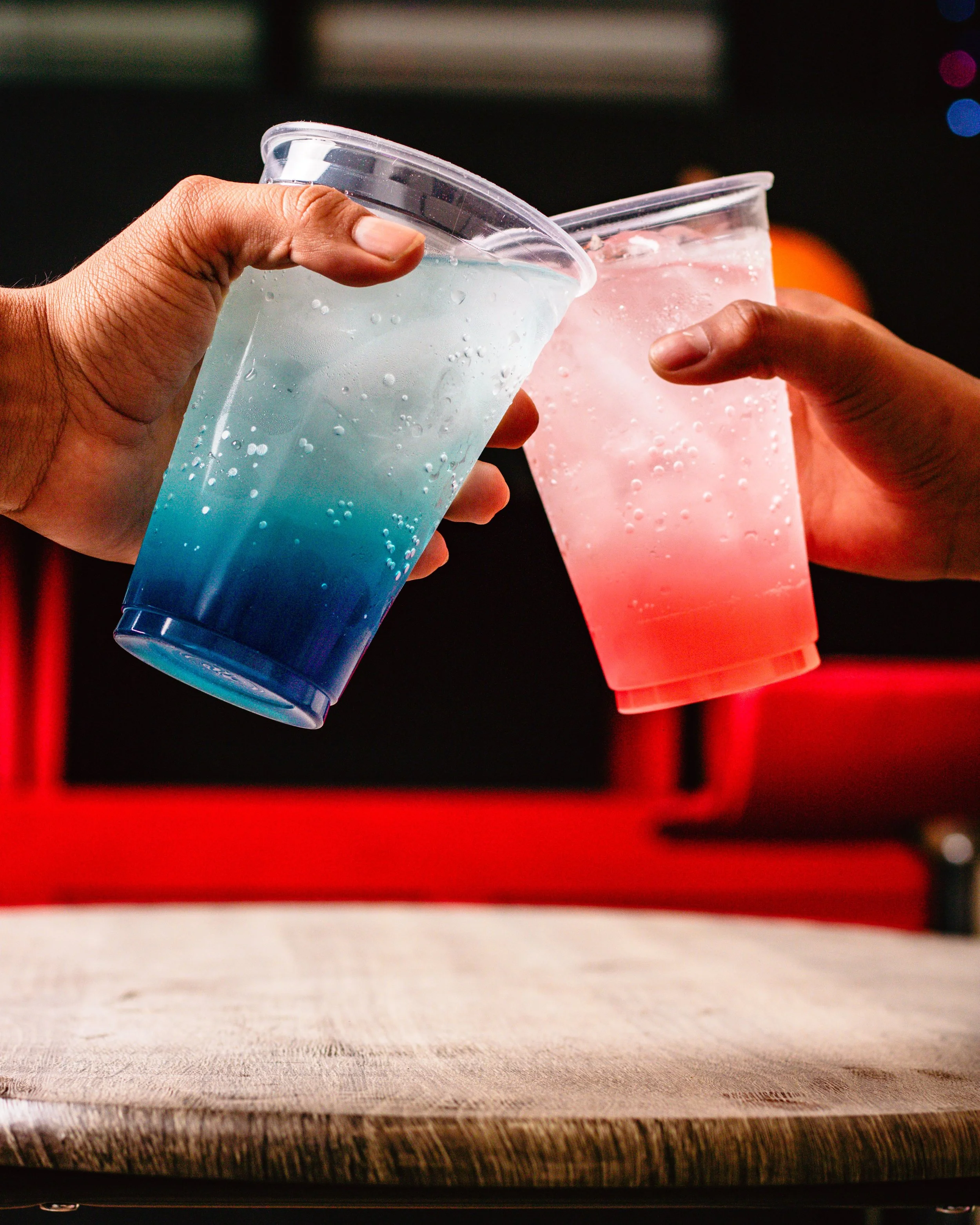 Two hands clinking colorful blue and pink dirty soda drinks together