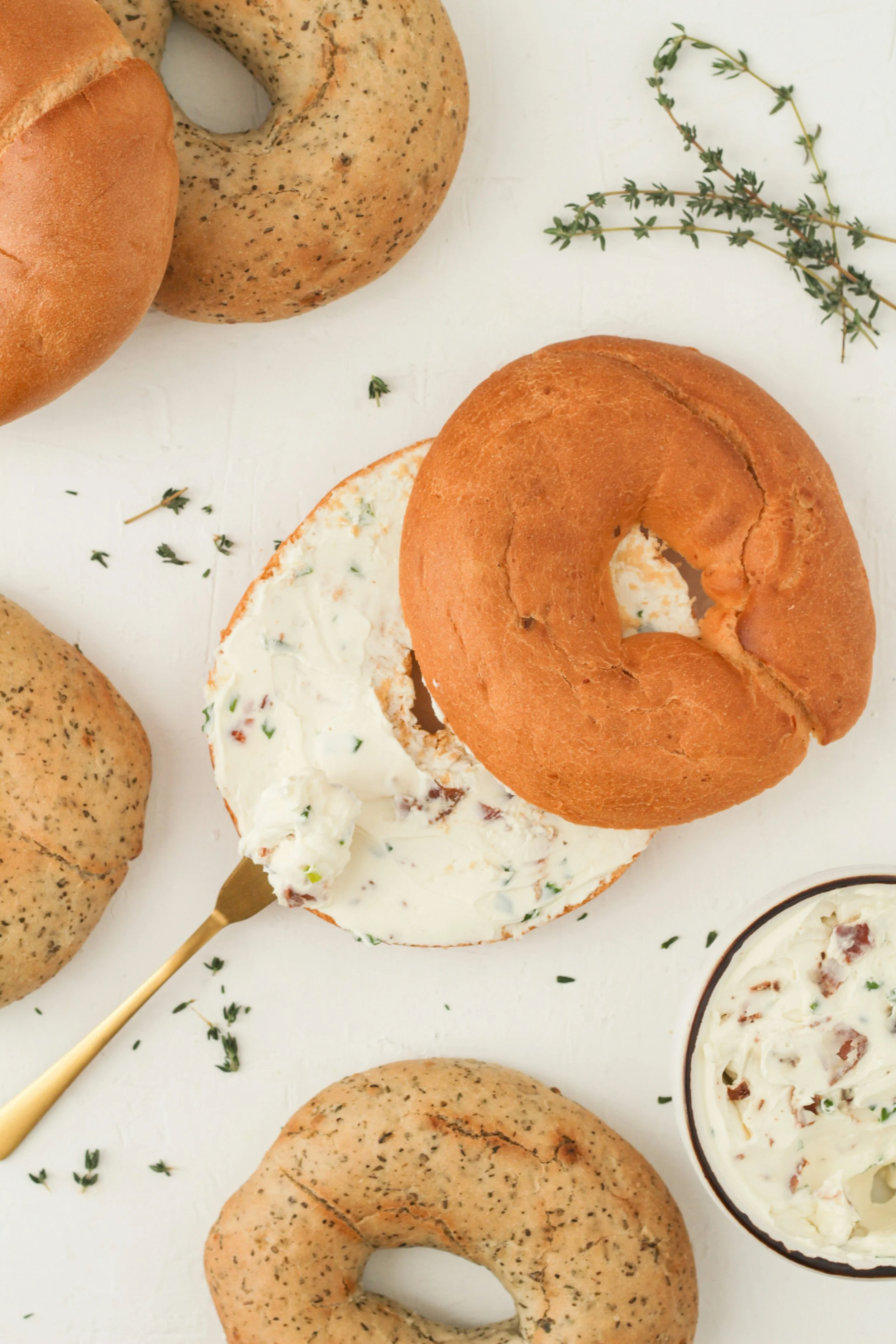 Bagels topped with cream cheese and herbs, served with a side of whipped spread