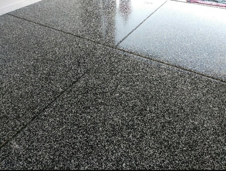 Close-up of a wet granite sidewalk with a textured surface.