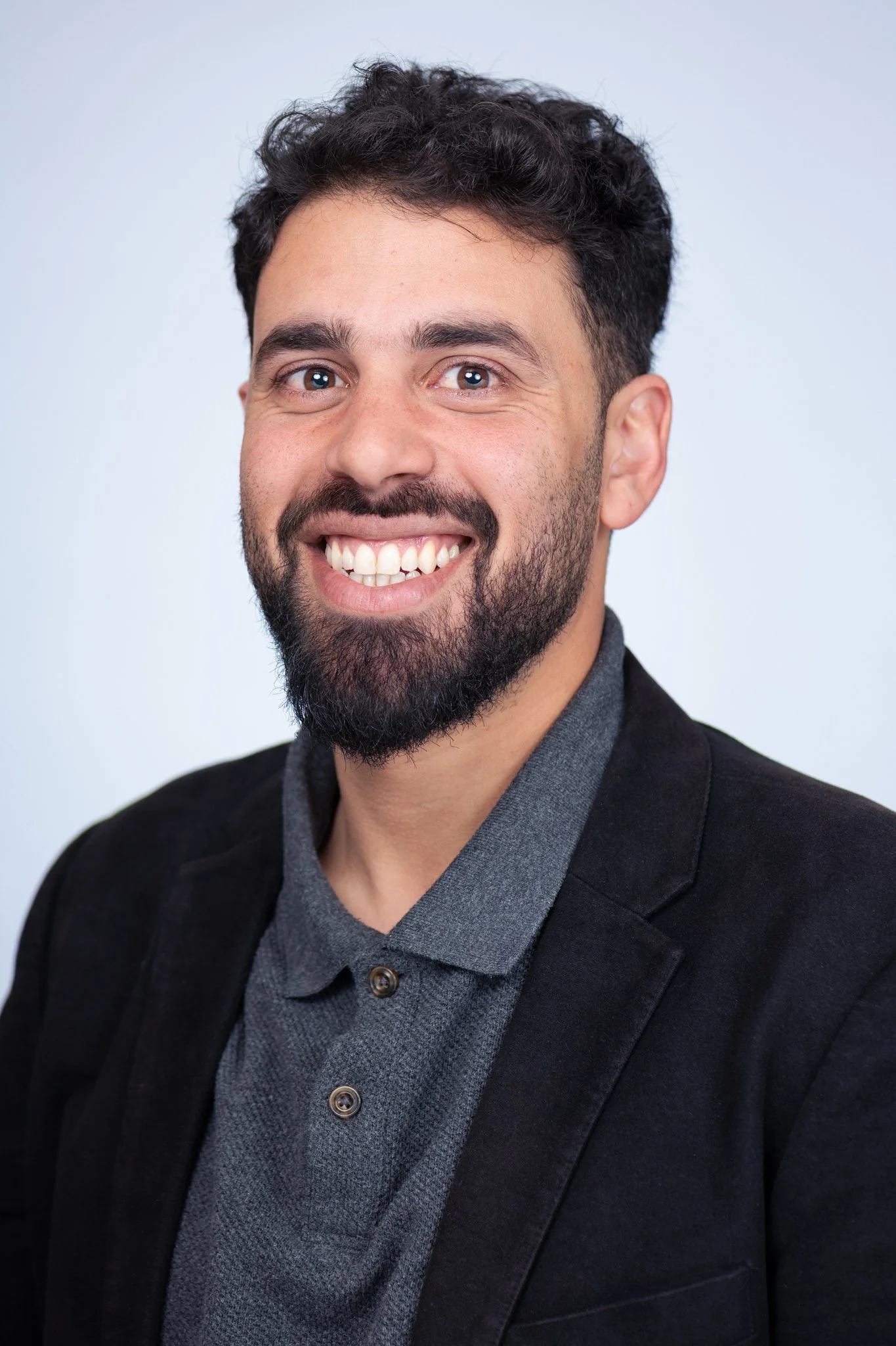 Headshot of Justin Ahmed, A smiling man with dark curly hair and a beard