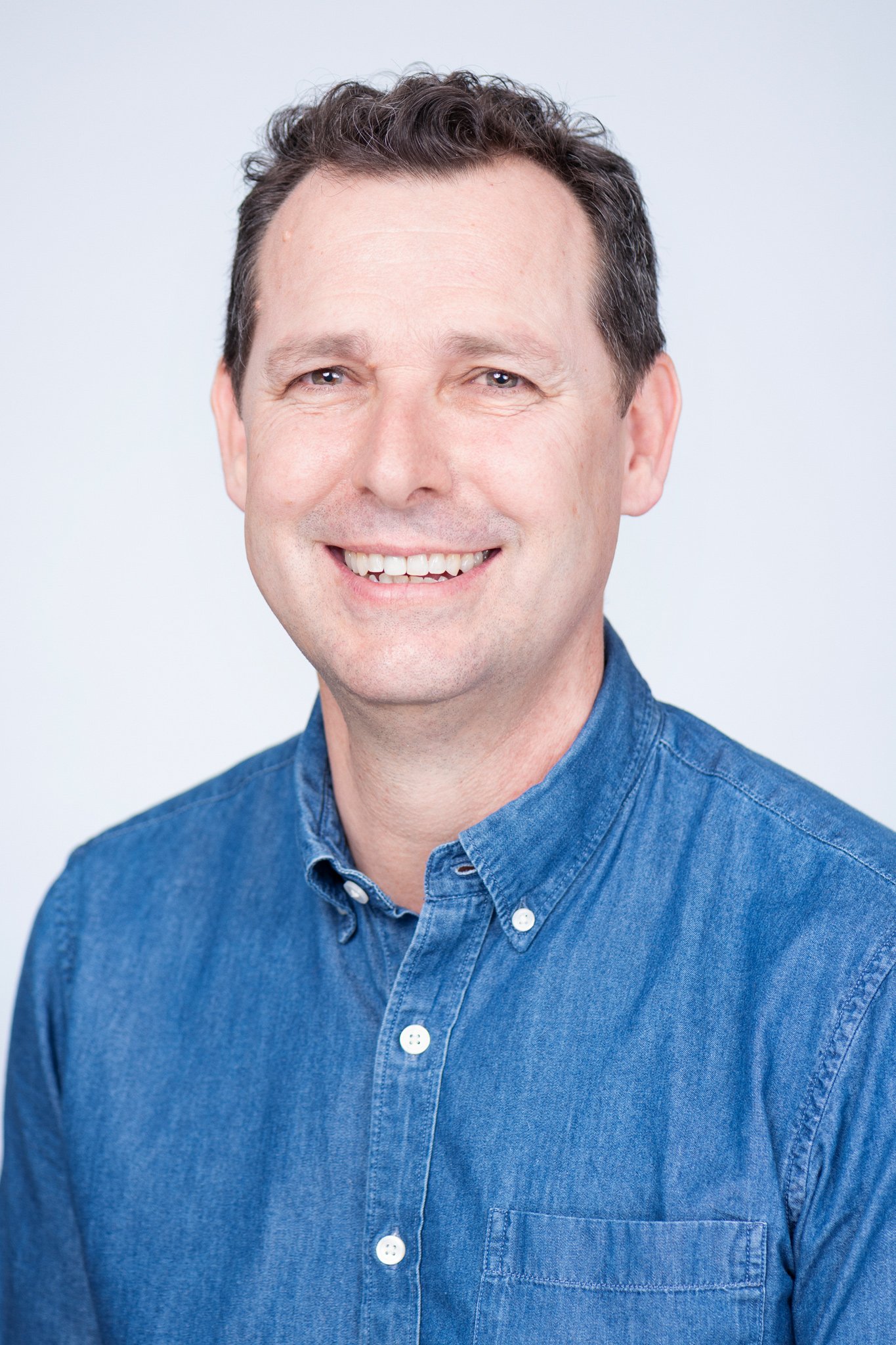 Headshot of Justin McMurray, a smiling man with short, curly dark hair wearing a blue button-up shirt