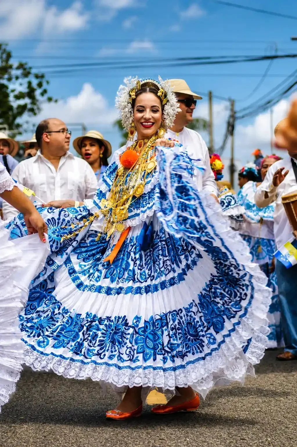 Vrouw in traditionele Mexicaanse klederdracht die danst tijdens een straatparade, omringd door mensen in witte kleding en hoed.