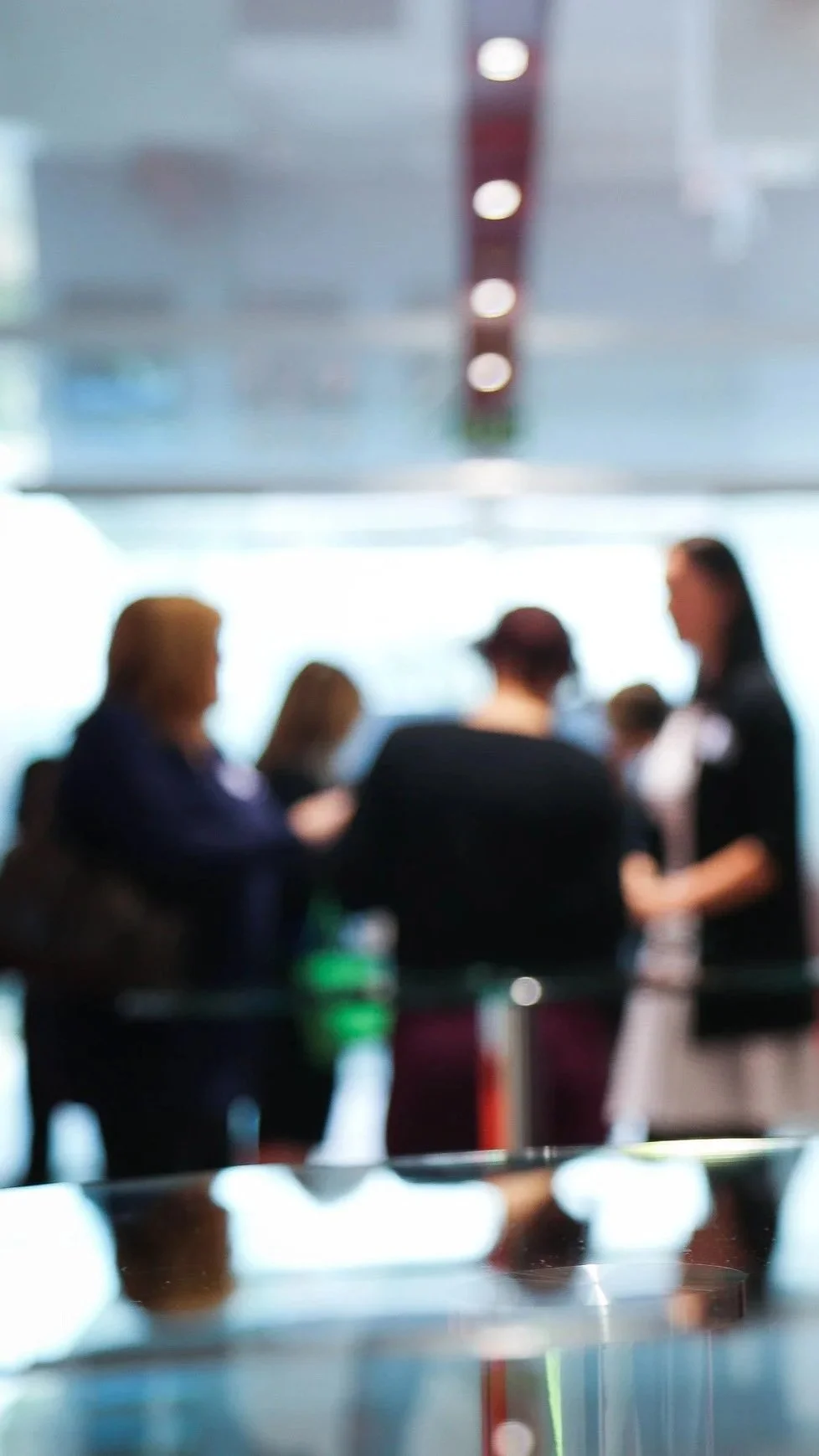Blurred image of a group of people standing and talking indoors, possibly at an airport or conference center.