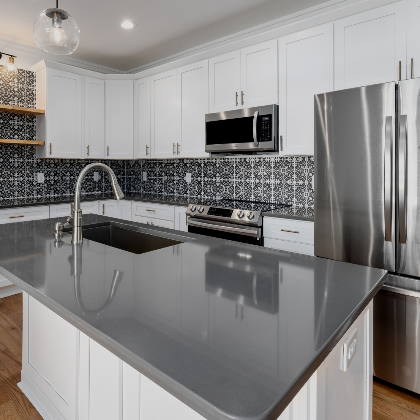 Modern kitchen with white cabinets, black and white patterned backsplash, stainless steel appliances, and a grey countertop island with a sink.