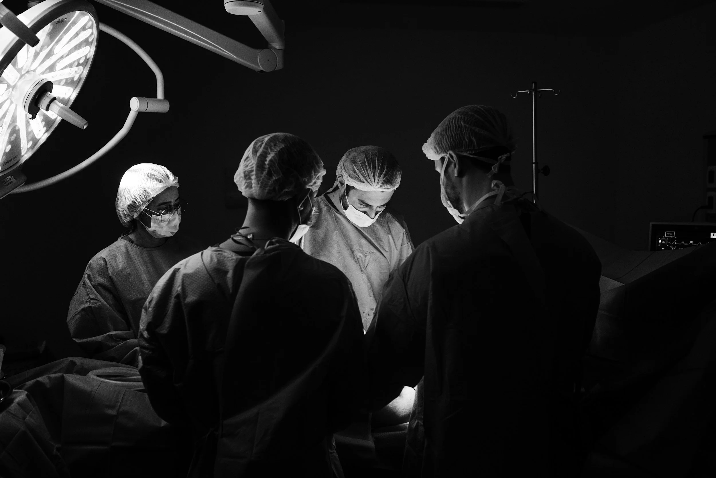 A team of surgeons and medical staff performing surgery in an operating room, with focused lighting, all wearing surgical masks and caps.