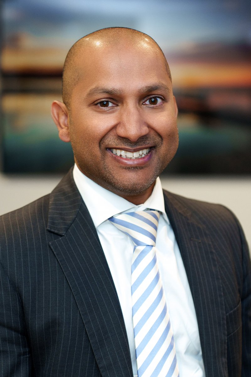 Smiling man in a suit and striped tie with a blurred cityscape background.