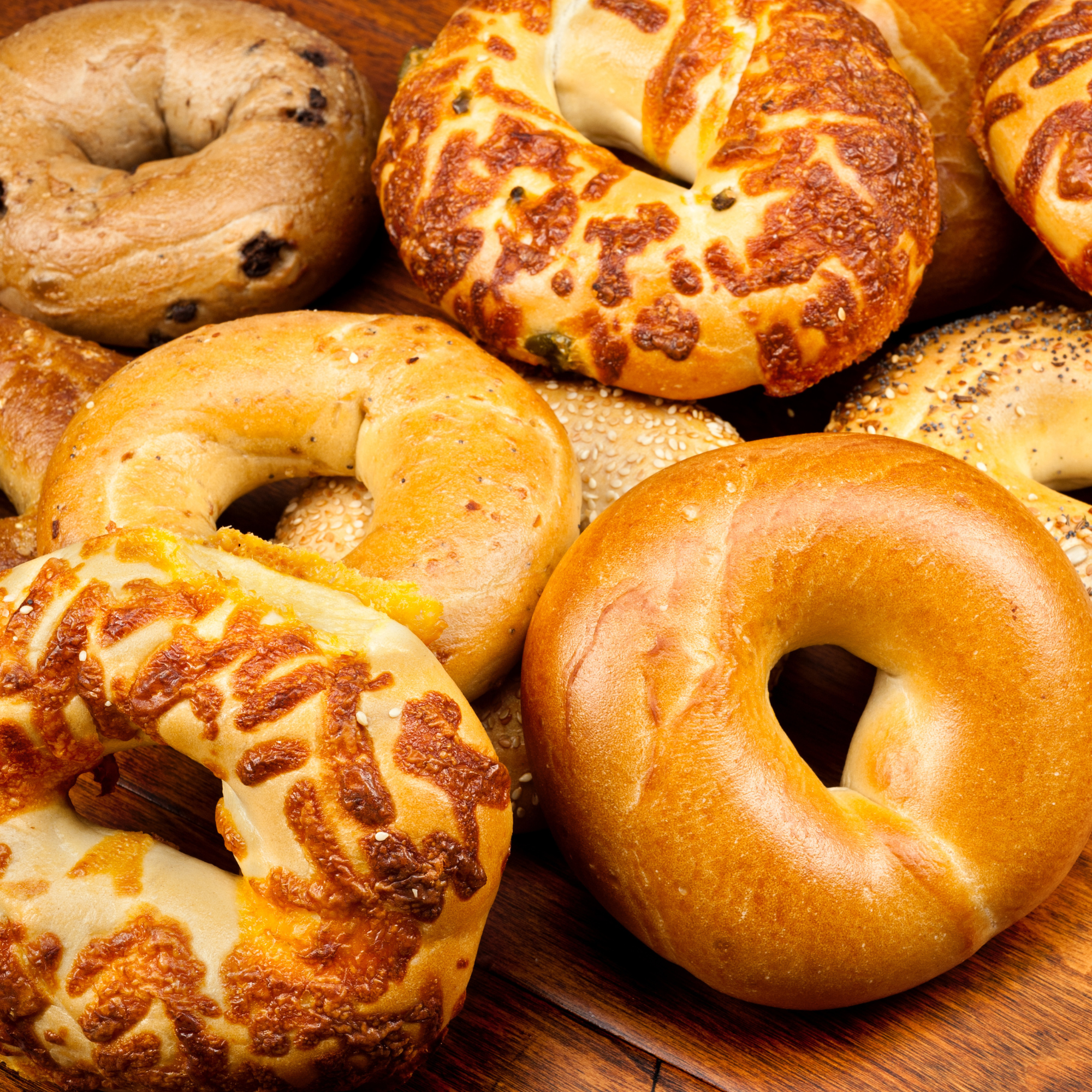 Assorted baked bagels with different toppings and flavors on a wooden surface.