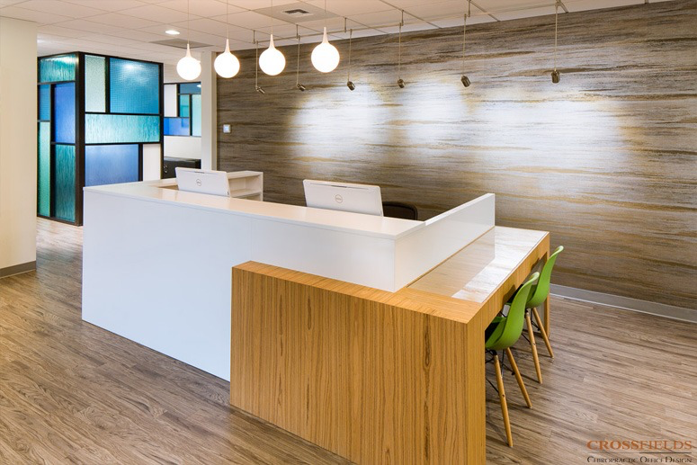 Modern office reception area with white curved desk, green chairs, wooden accent wall, and pendant lighting
