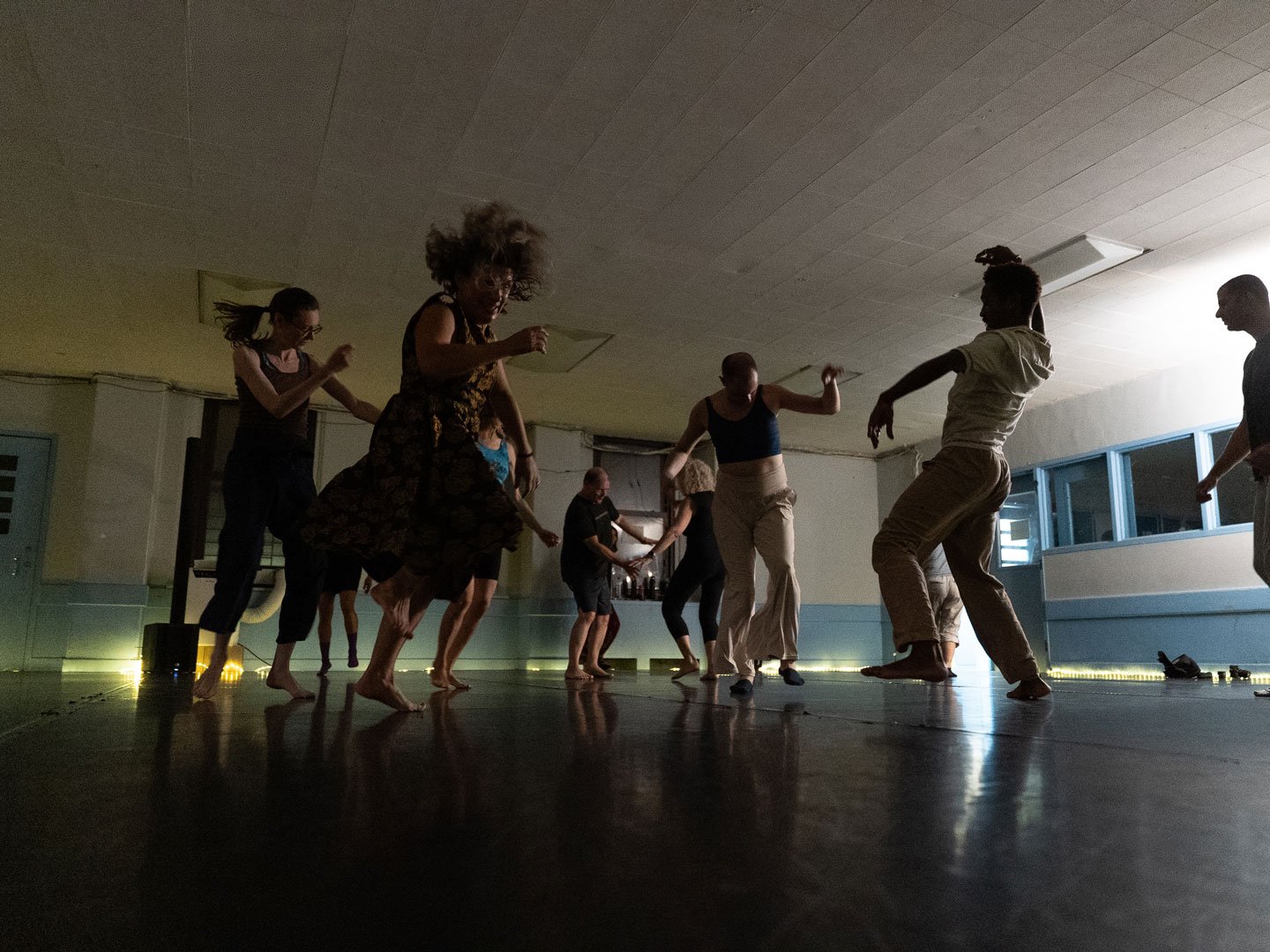 Group of diverse dancers performing in a dimly lit studio with polished floors