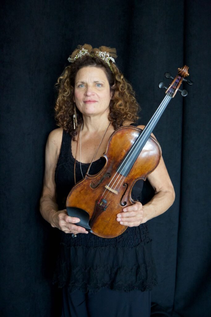 Karen in a black dress holding a wooden violin against a dark backdrop