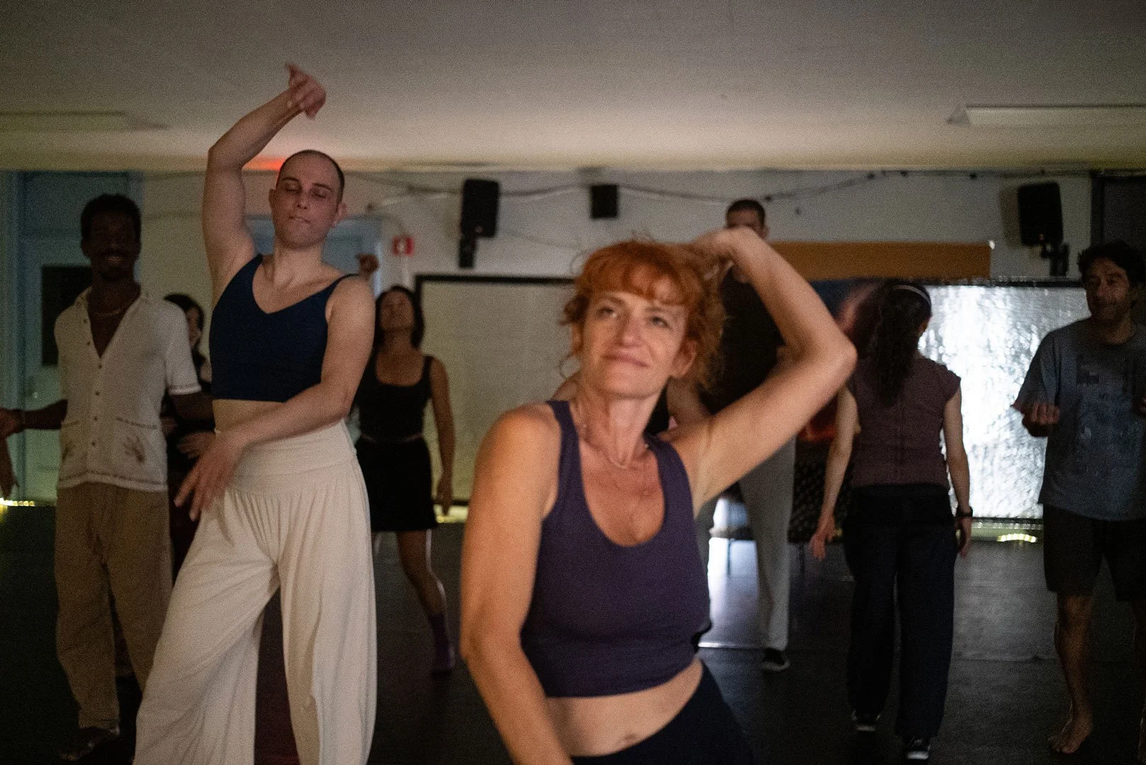 Group of people dancing in a dimly lit studio, with two women posing in the foreground.