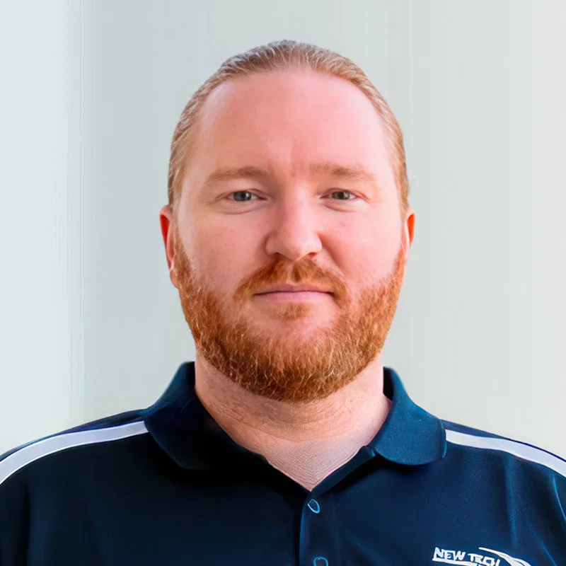 Portrait of a man with red hair and beard, wearing a navy blue polo shirt with white stripe details.