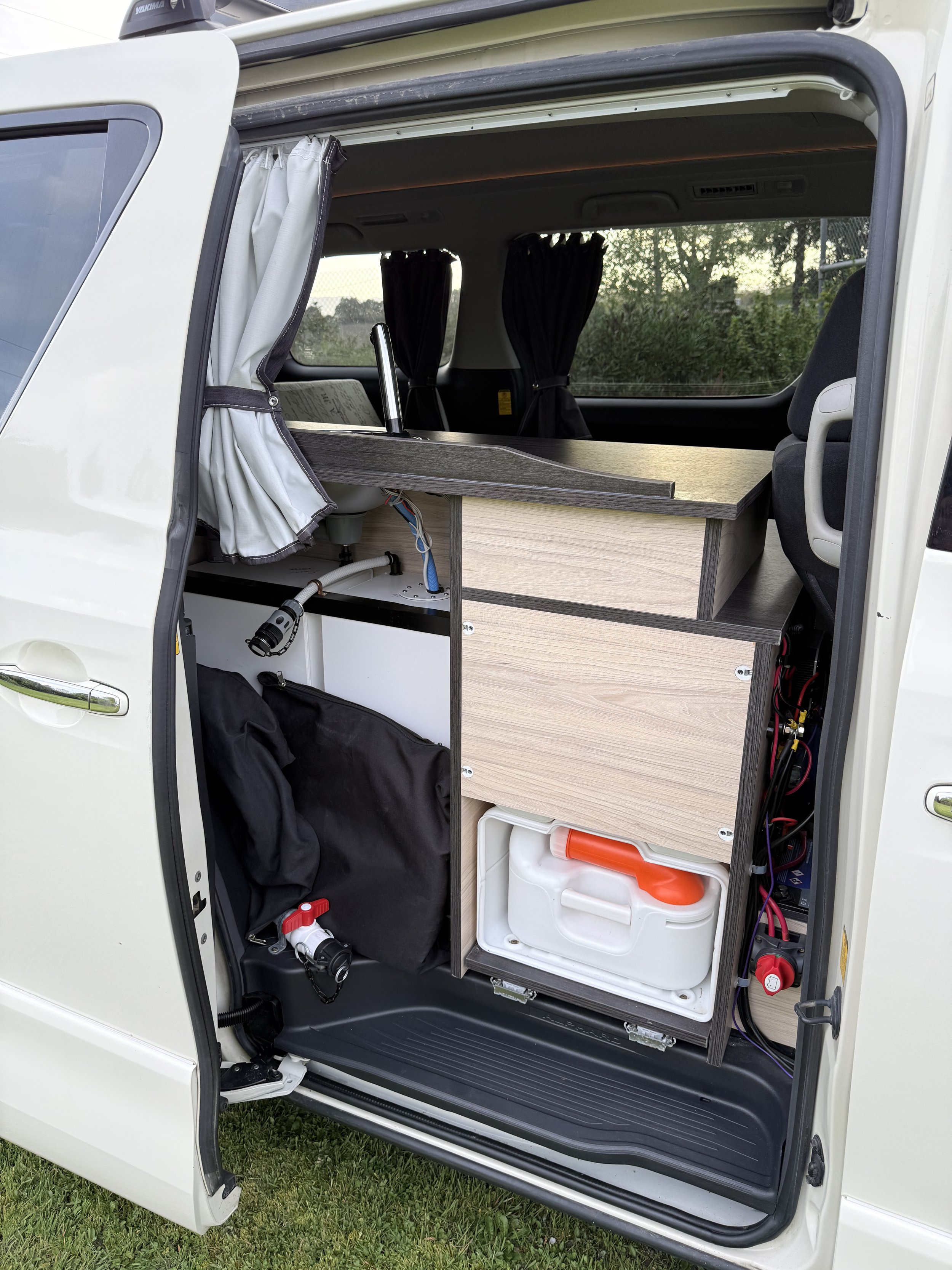 The interior of a camper van showing organized storage with wood paneling, a small water container, and various equipment and supplies.
