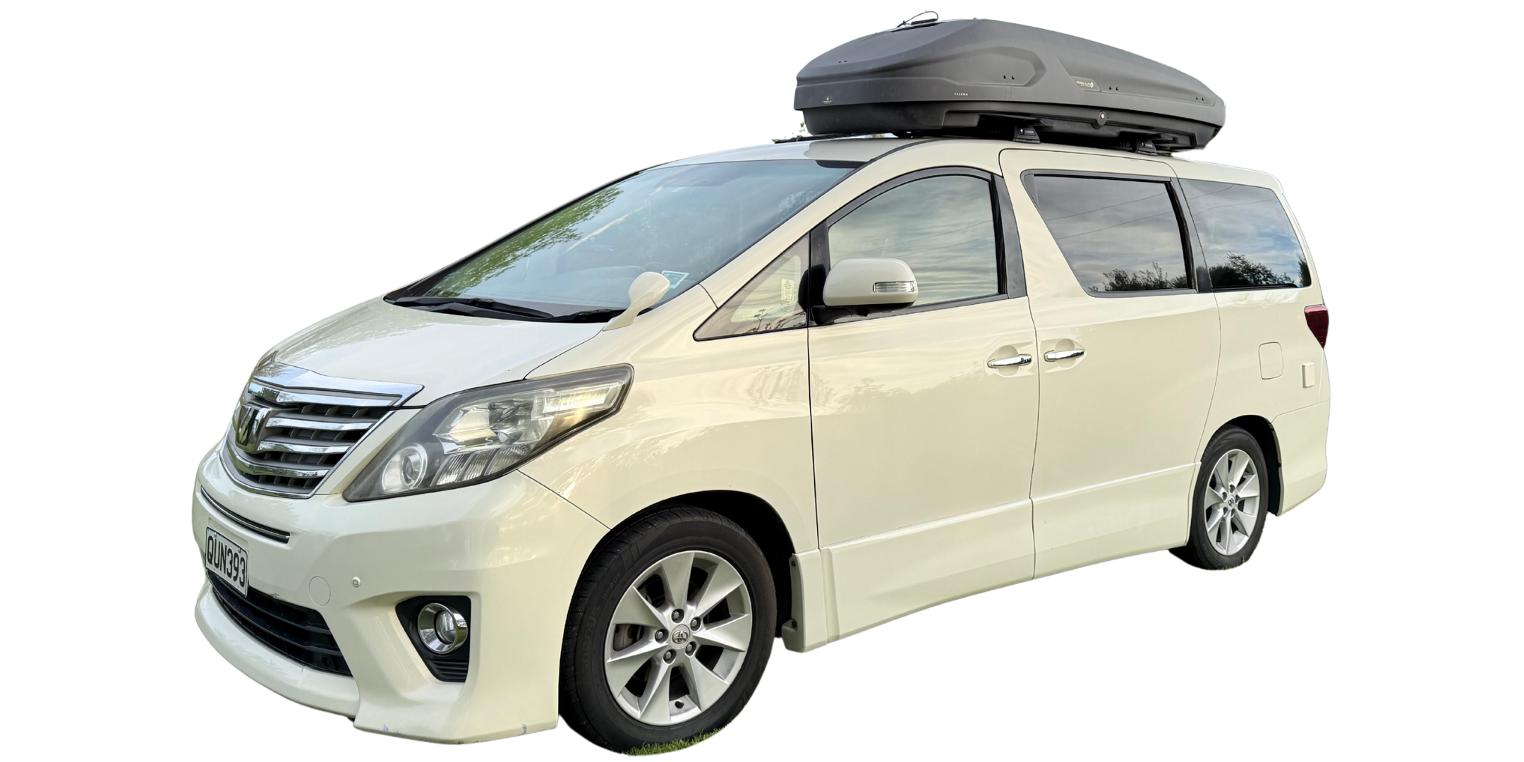 A white minivan in New Zealand from Go Beyond Campers with a roof cargo box parked outdoors, with trees reflected in the tinted windows.