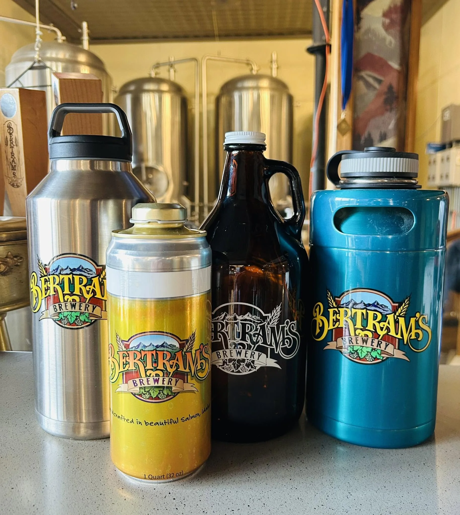 Various bottles of beverages, including aluminum and glass bottles, placed on a countertop with fermentation tanks in the background at Bertram's Salmon Valley Brewery