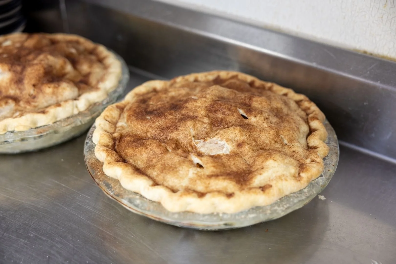 Two homemade apple pies with golden brown crusts rest on metal trays in the Bertram's kitchen.