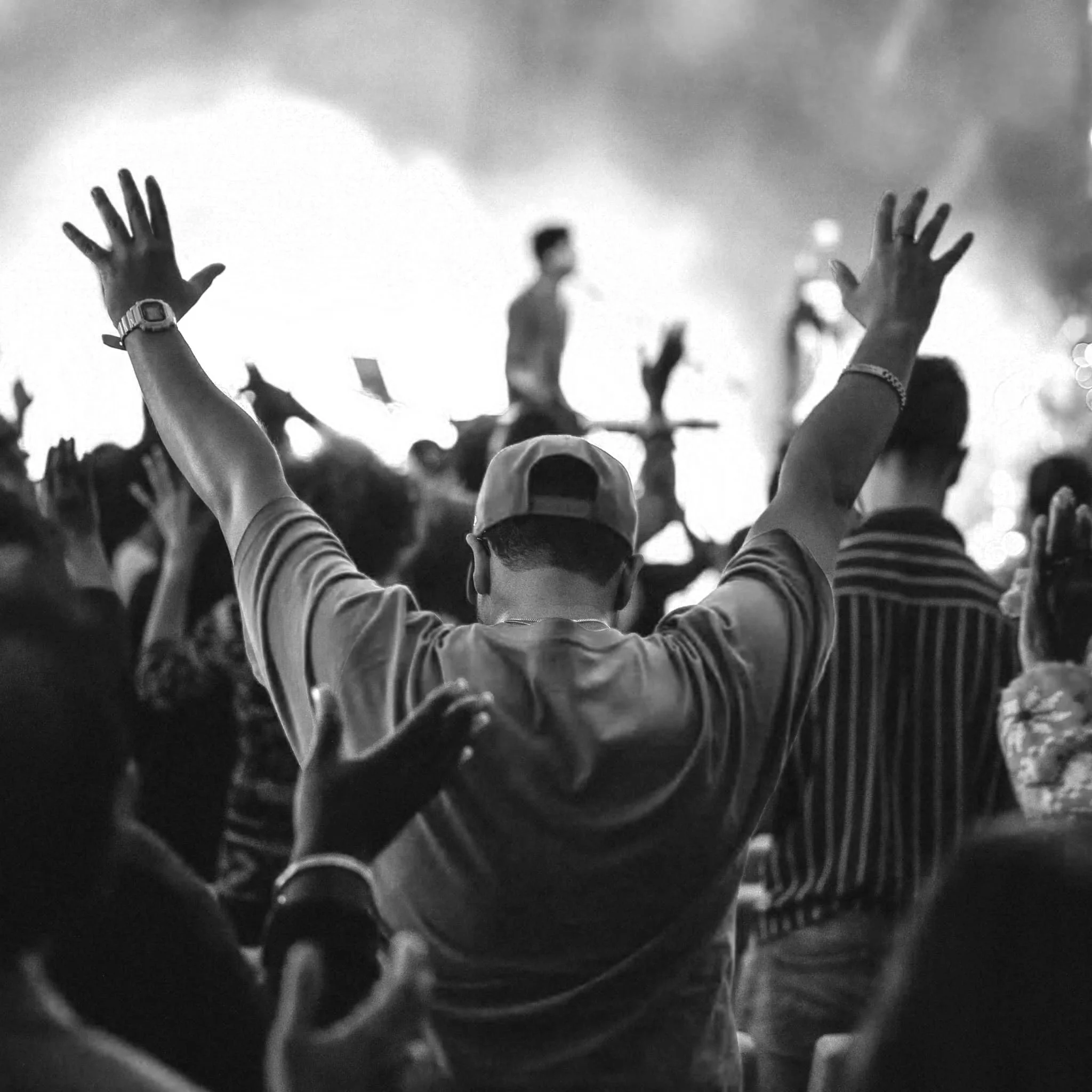 A crowd of people with their hands raised during a concert or event, with some wearing watches and bracelets.