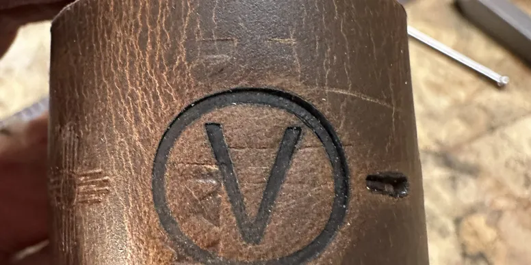 Close-up of a wooden surface with a circular logo containing the letter 'V' engraved or stamped onto it.