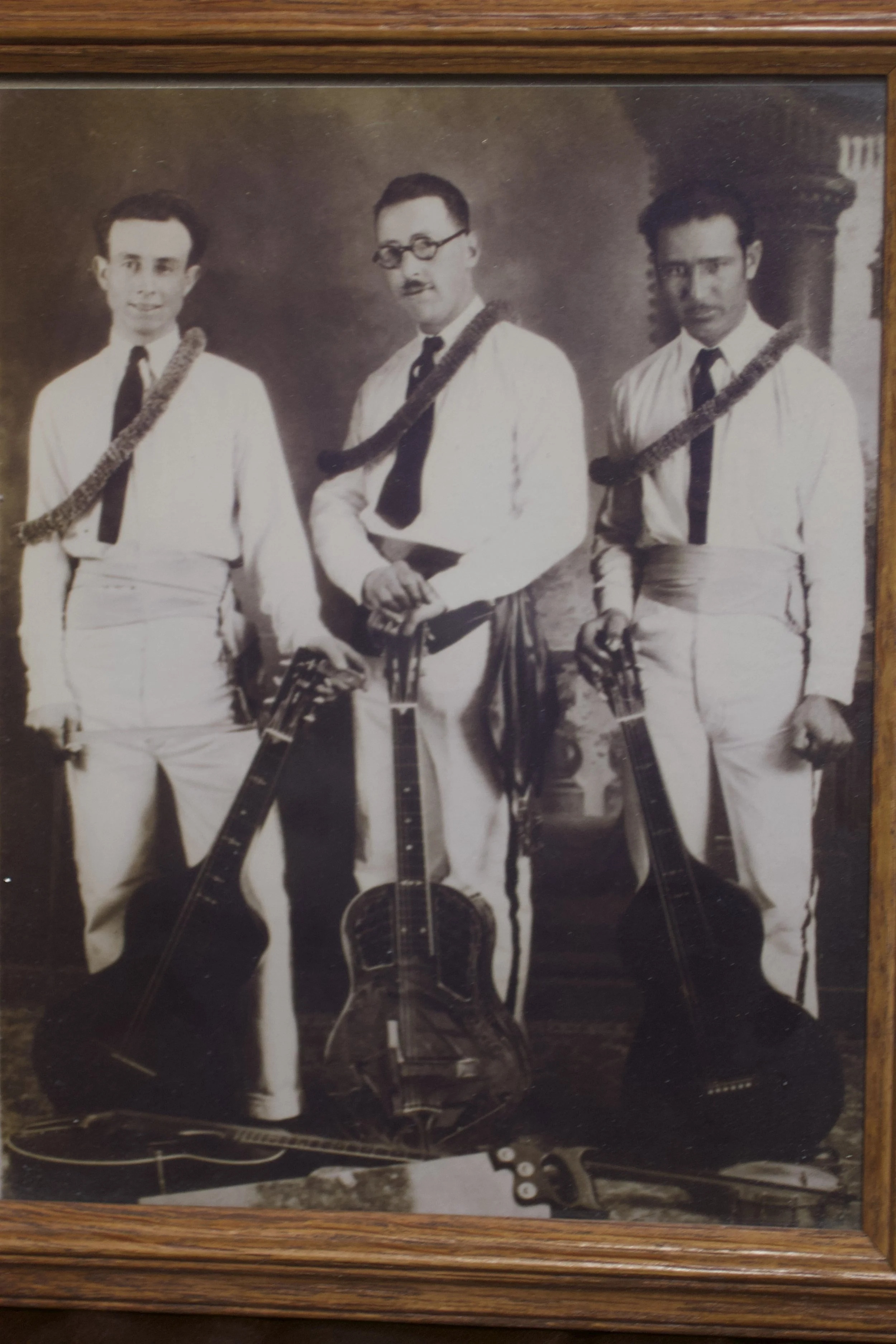 Black and white photograph of three young men in formal attire, each holding a musical instrument, in a studio setting.