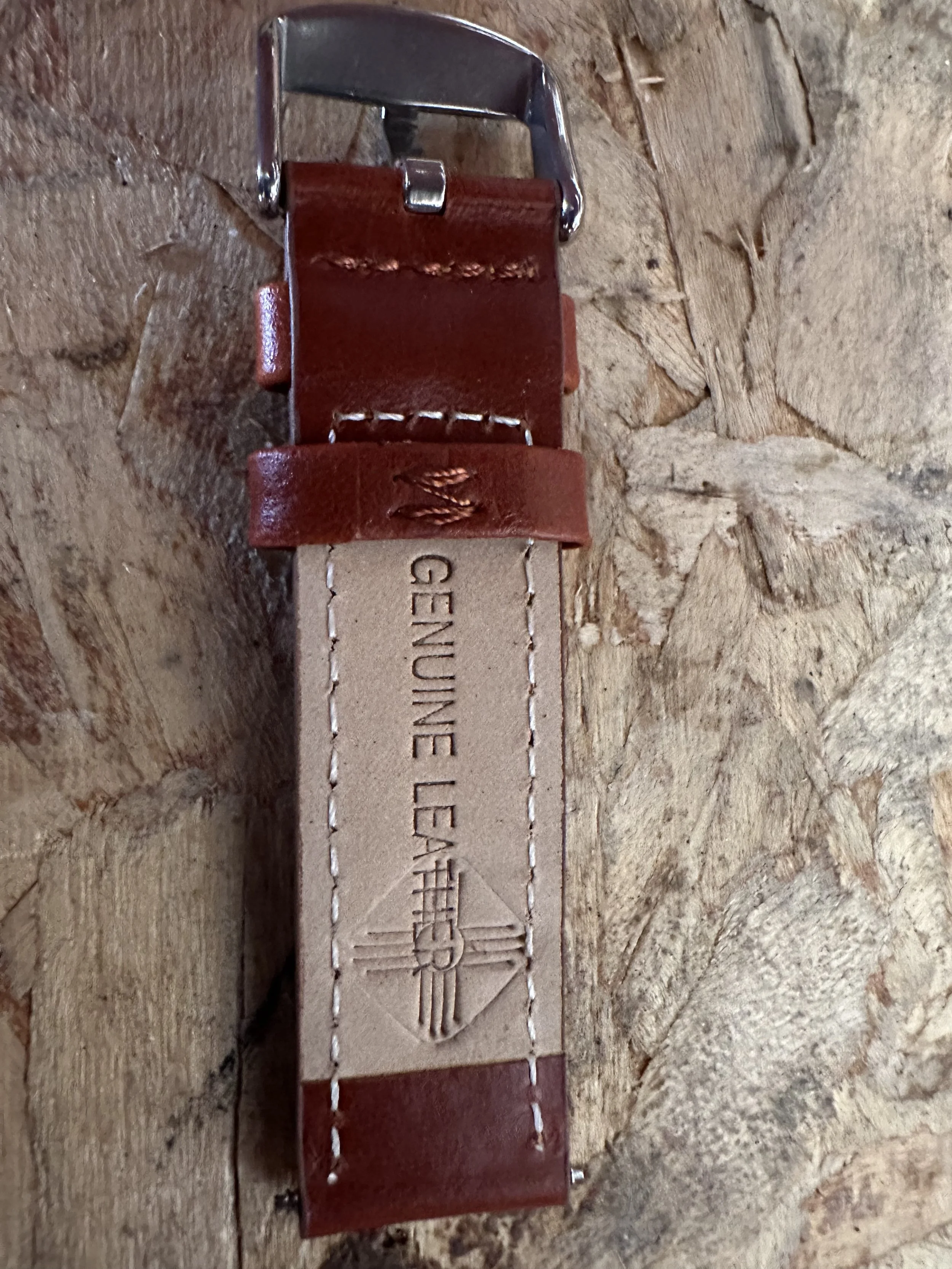 Leather tag with embossed text and a metal buckle, attached to a piece of leather, on a rough wooden surface.
